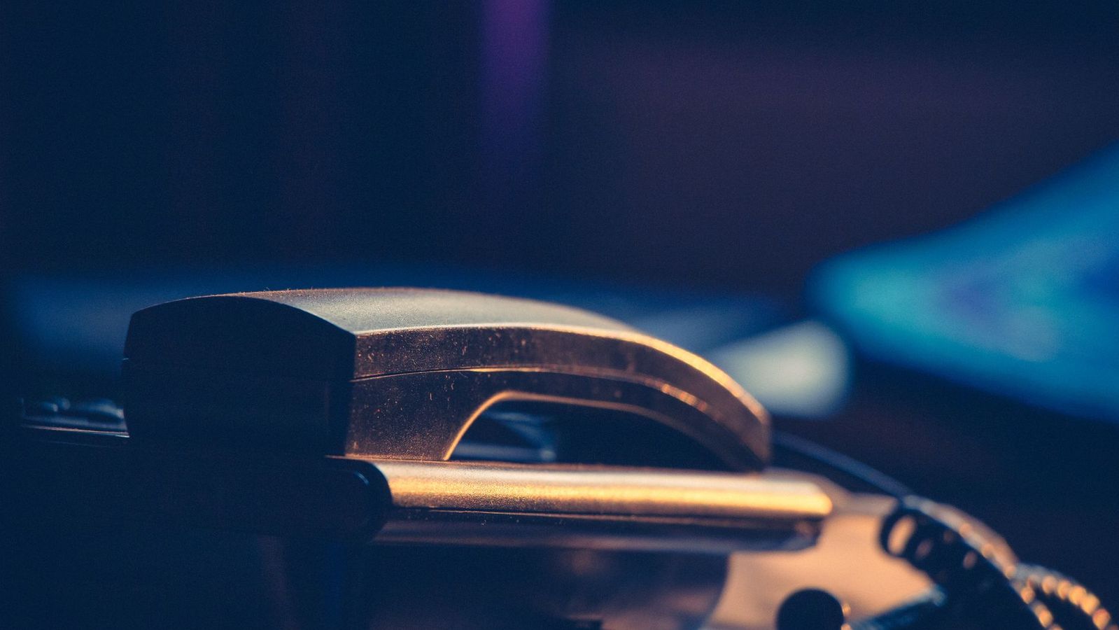 Close up of a telephone handset resting in its cradle, lit by warm light against a dark blue background.