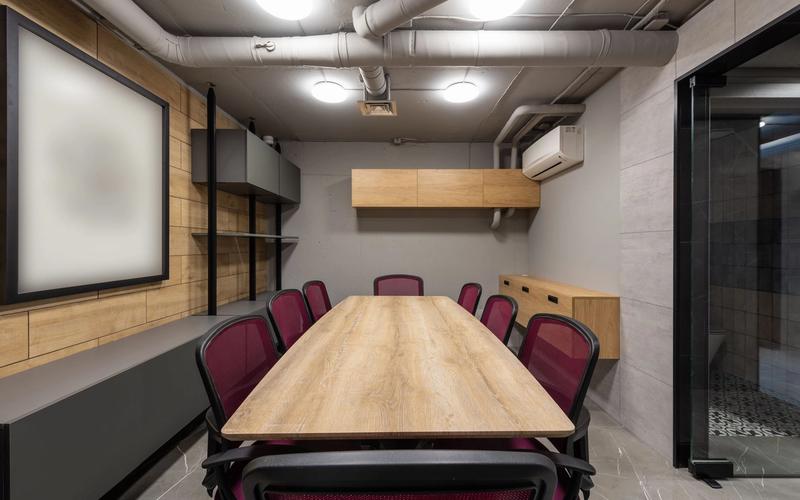 A modern meeting room with a large wooden table and office chairs, lit by ceiling lamps.