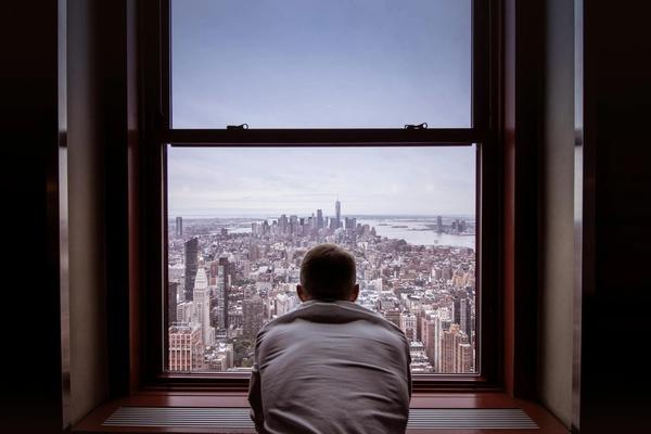 A man stands by a large window overlooking a city skyline in daylight.