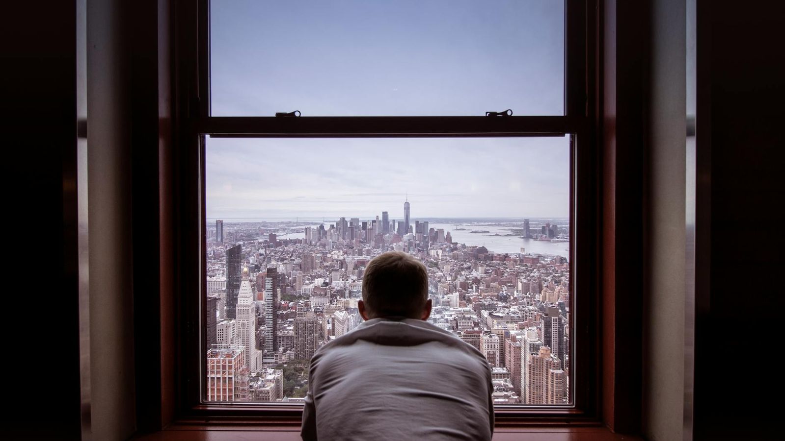 A man stands by a large window overlooking a city skyline in daylight.