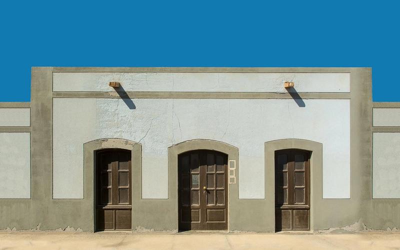 A symmetrical facade with three wooden doors under a clear blue sky.