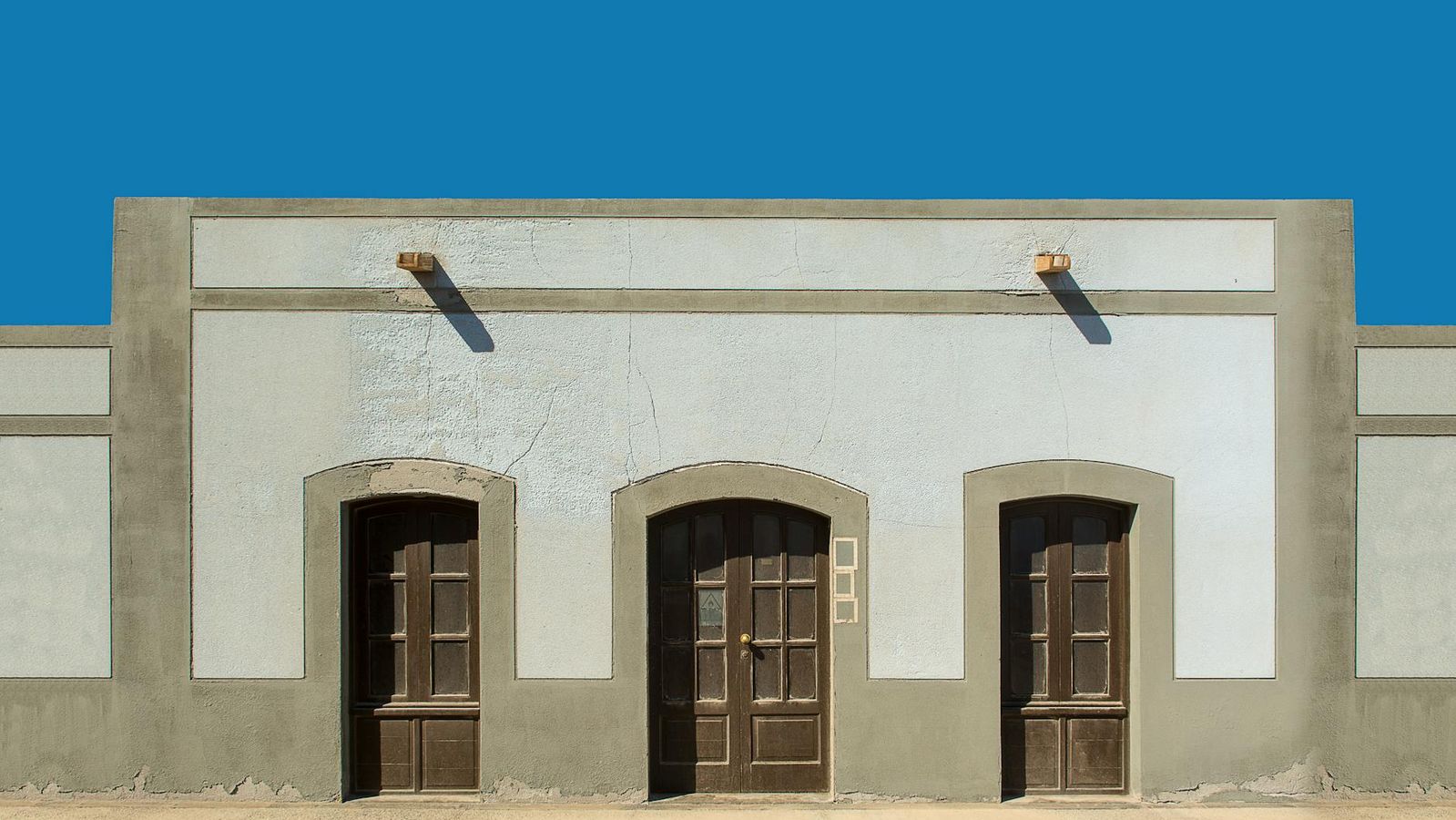 A symmetrical facade with three wooden doors under a clear blue sky.