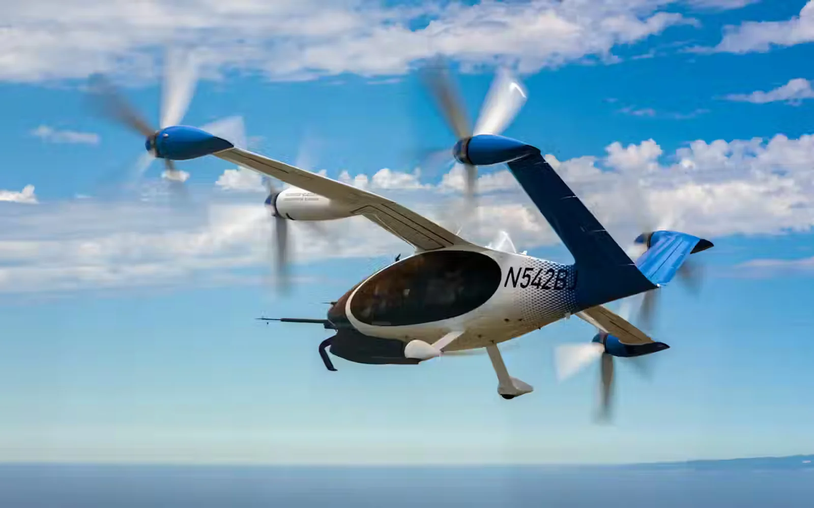 Joby aircraft flies through a blue sky, the ocean skyline in the background