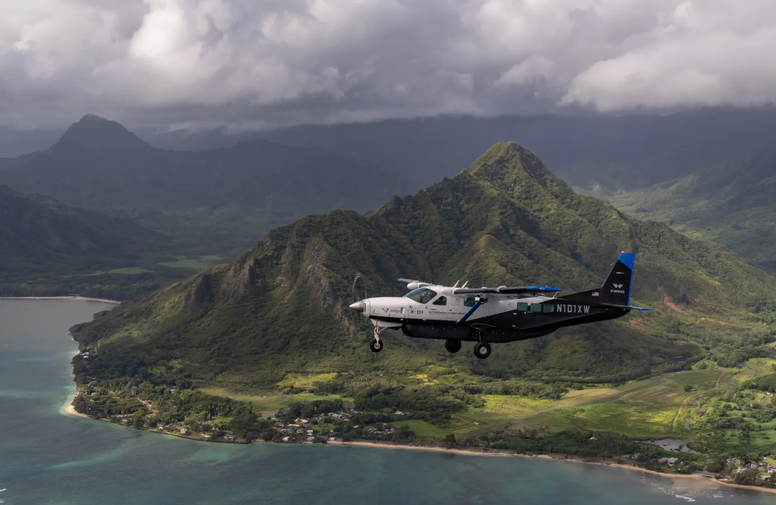 Small autonomous plane flies over green Hawaii island mountains and the ocean