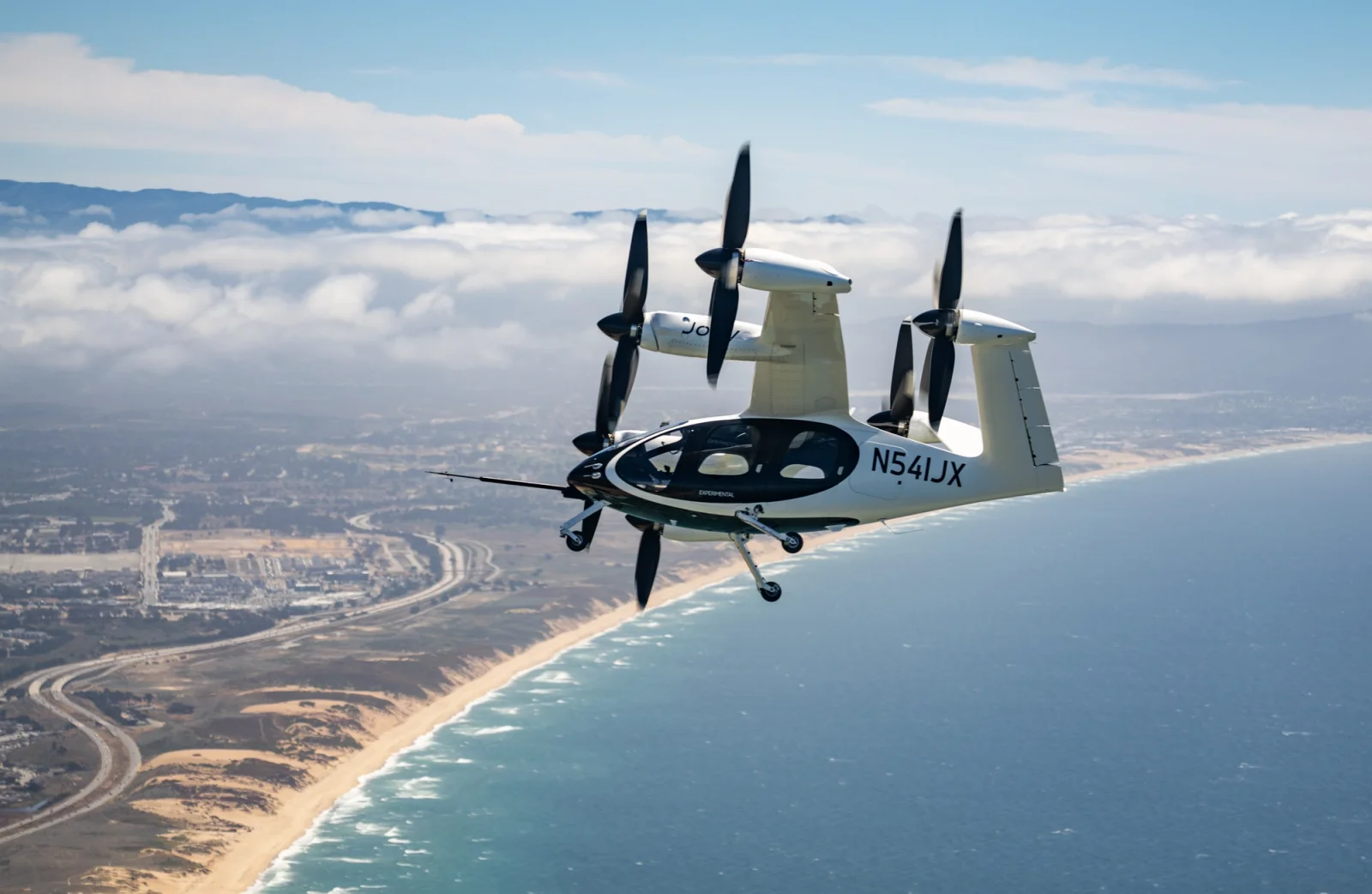 Joby aircraft soars high above the ocean, clouds visible in the background