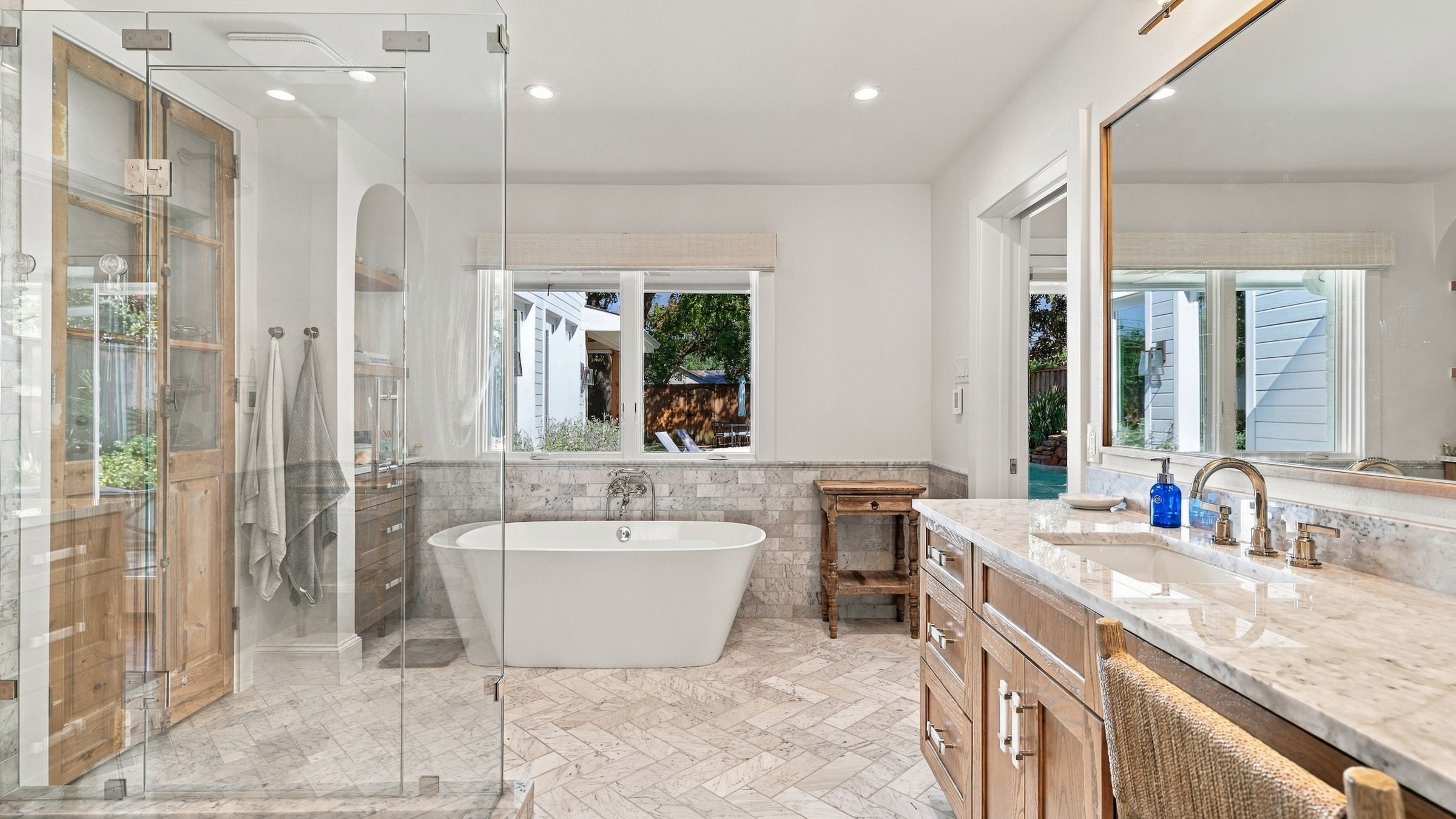 Primary bath after: a freestanding tub, a glass shower and a stained wood vanity