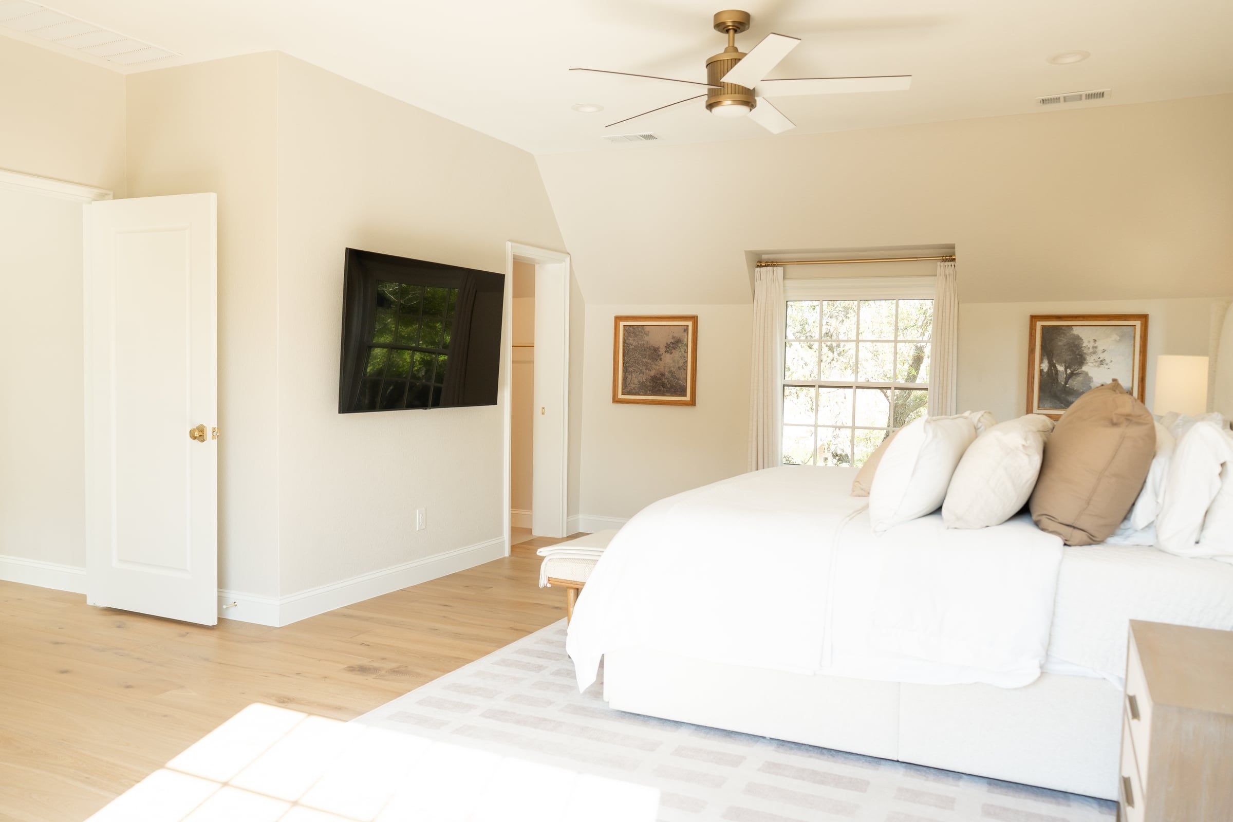 Primary bedroom with a wall-mounted television, tall windows and white oak floors