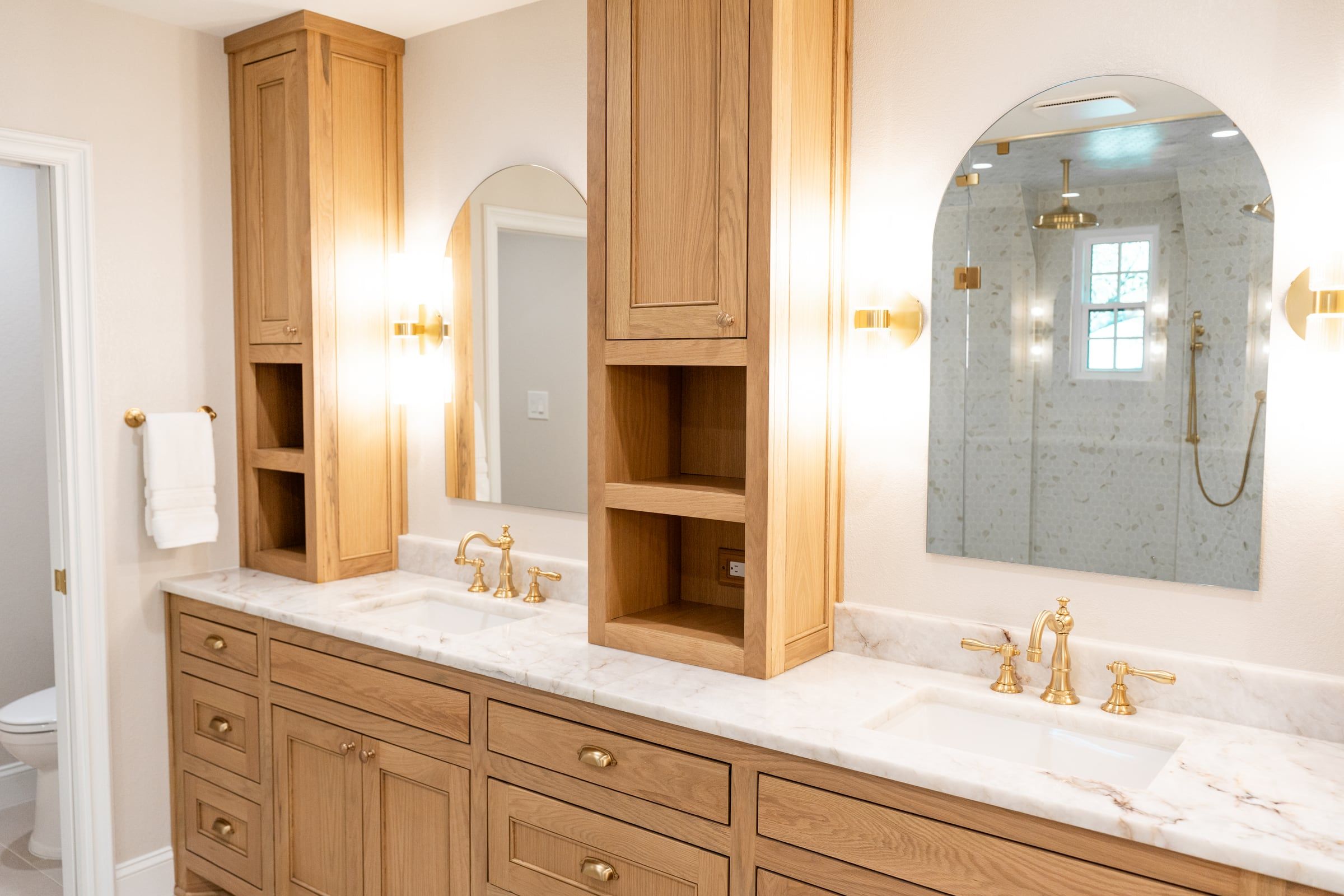 Primary bathroom with a white oak double vanity, marble counters and an arched shower