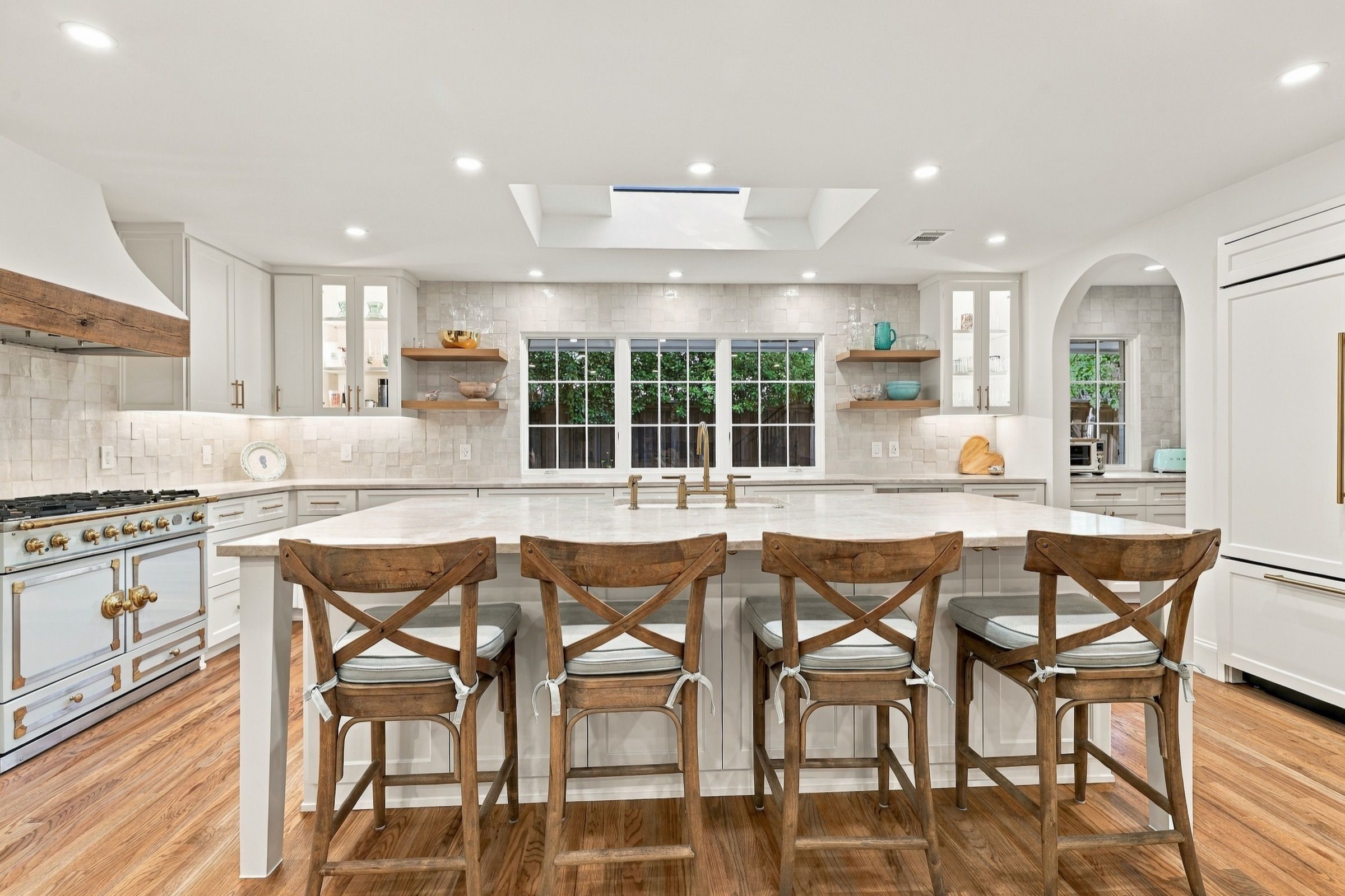 Kitchen island with four wood stools, a white range hood and open shelves around the windows