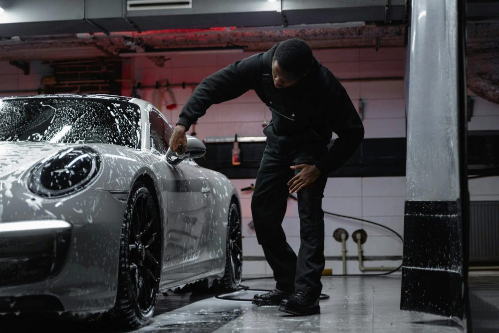Handtvätt av skumtäckt silverfärgad Porsche i en mörk tvätthall