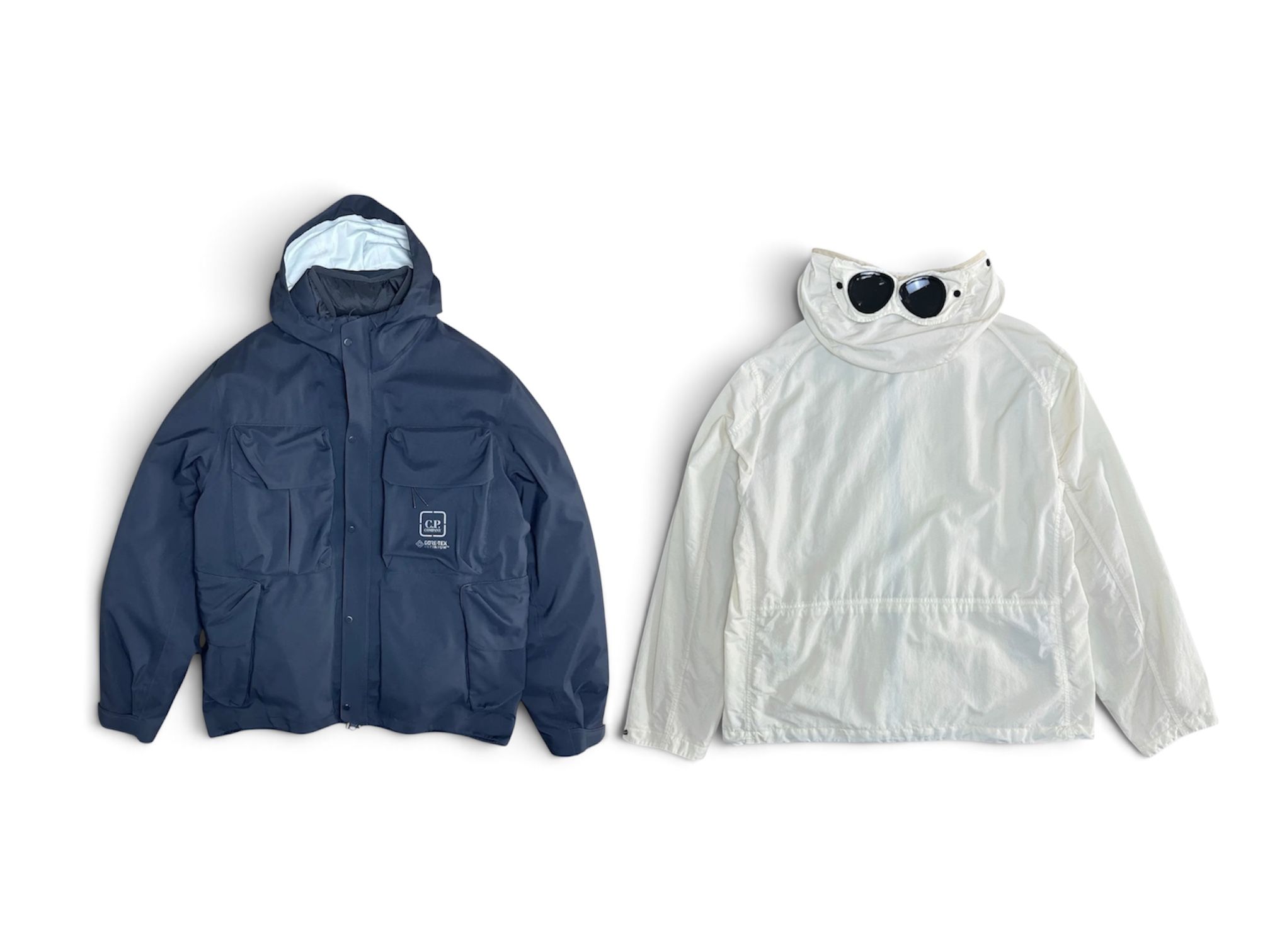 Front of flat layed blue C.P. Company jacket and the back of a flat layed C.P. Company goggle jacket