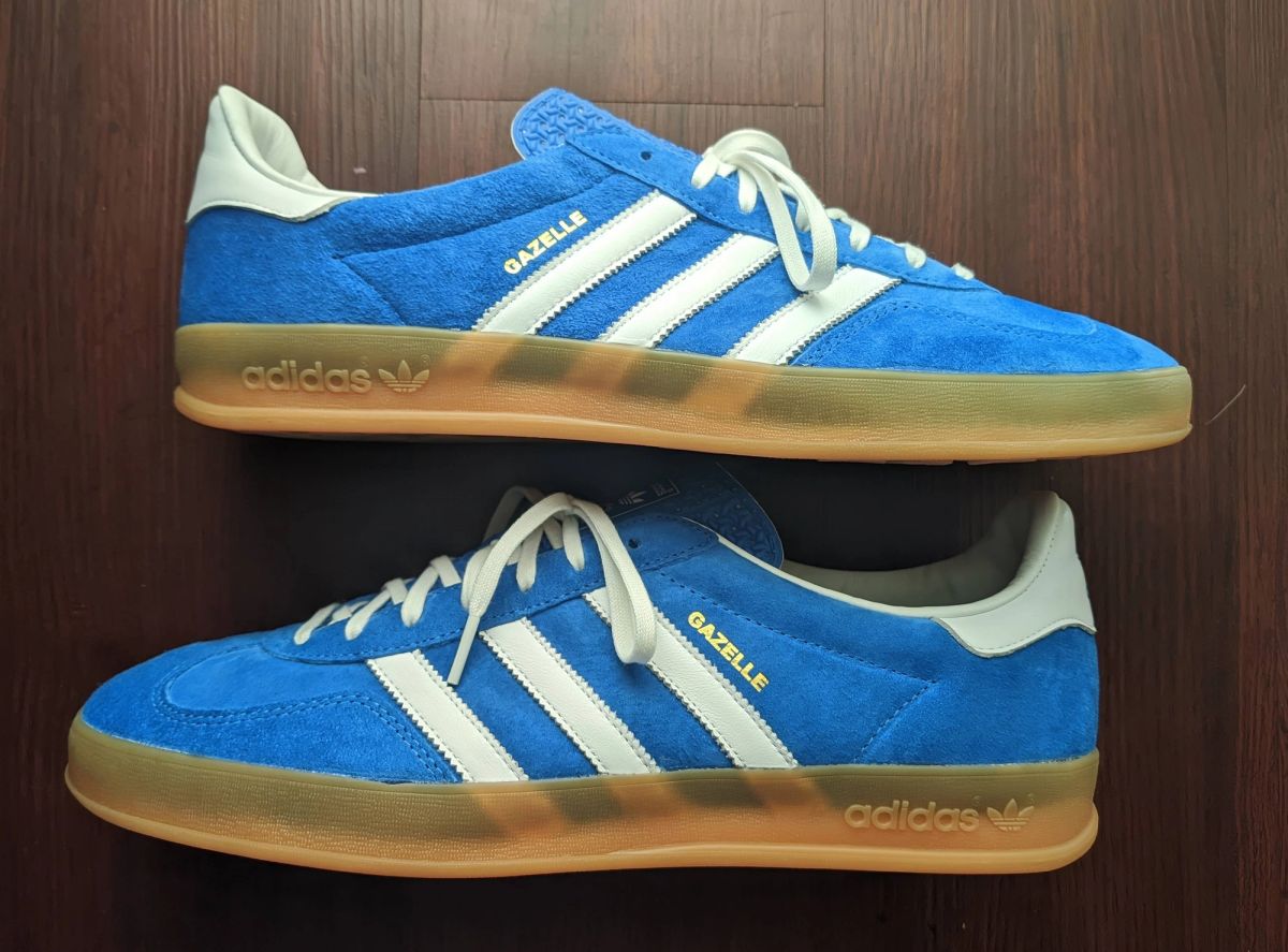 A pair of blue suede Adidas Gazelle trainers with white stripes and a gum sole