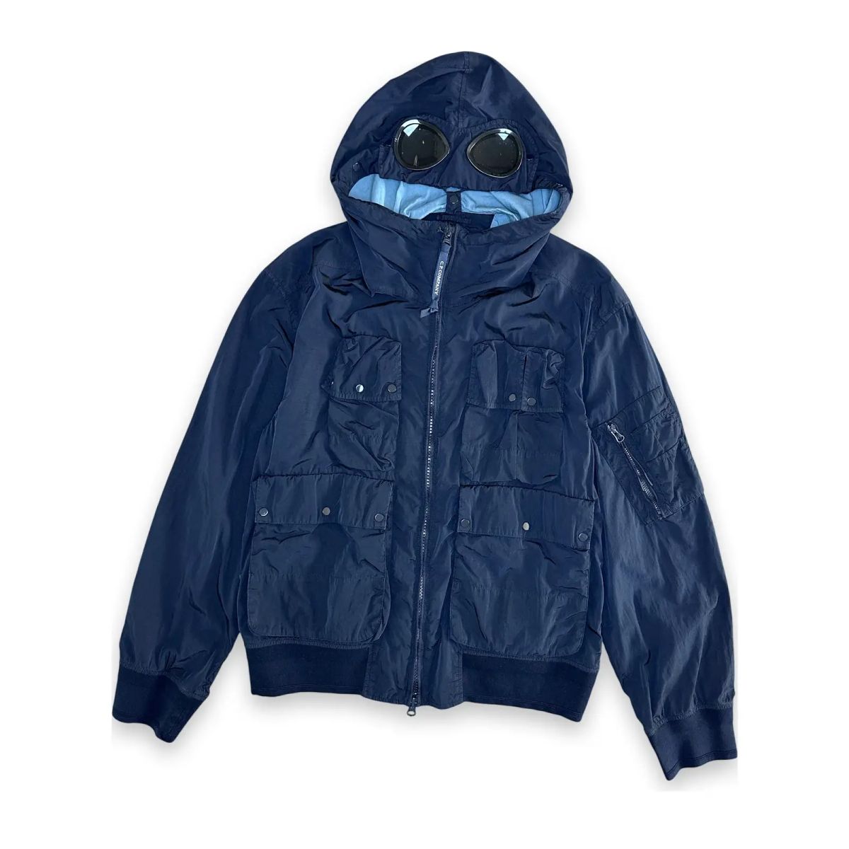Flat lay of a navy C.P. Company chrome-r jacket with iconic goggles in hoodie