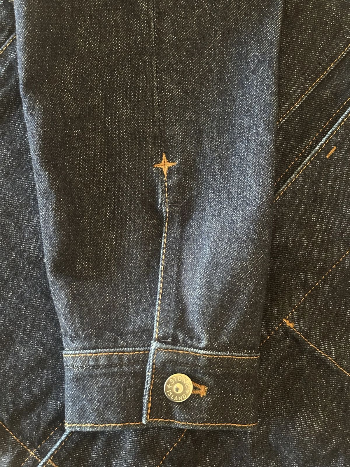 Close-up van de manchet van een Stone Island denim jas met geborduurde kompasster en een gemerkte knoop