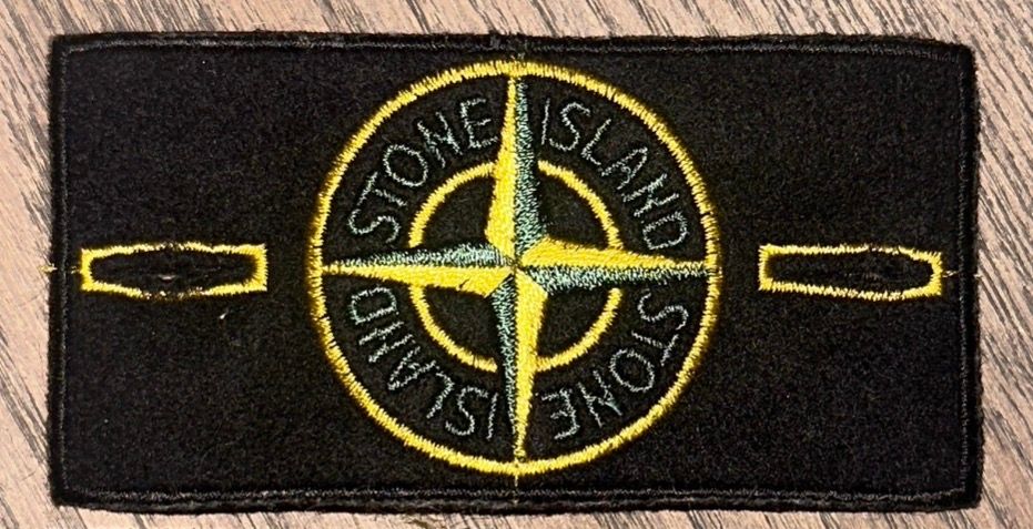 Close-up of a genuine Stone Island compass badge, embroidered in yellow and green on black felt