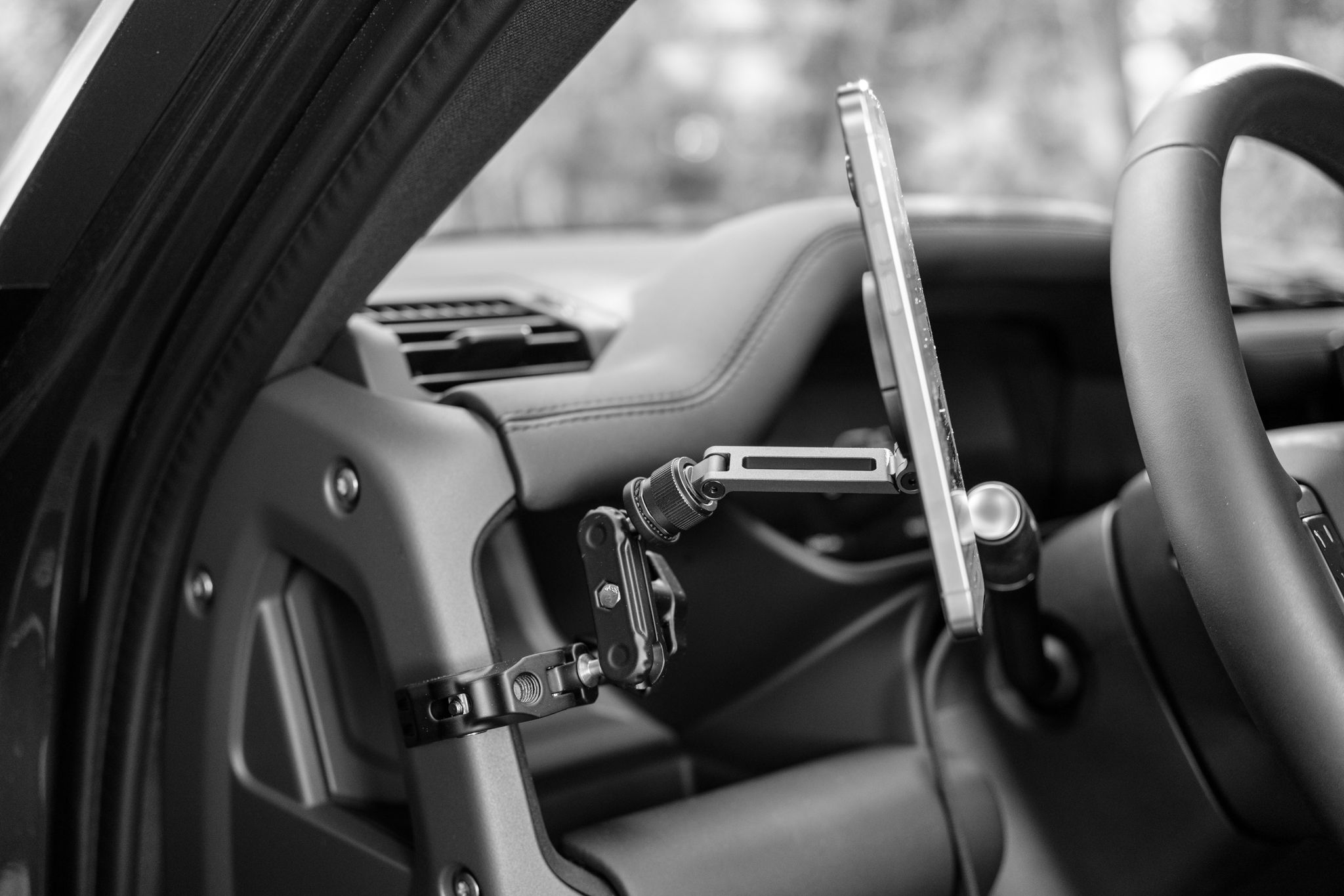 Land Rover Defender phone mount setup using a ULANZI Super Clamp and MagSafe magnetic mount attached to the driver's side A-pillar grab handle, viewed from the side with a phone attached