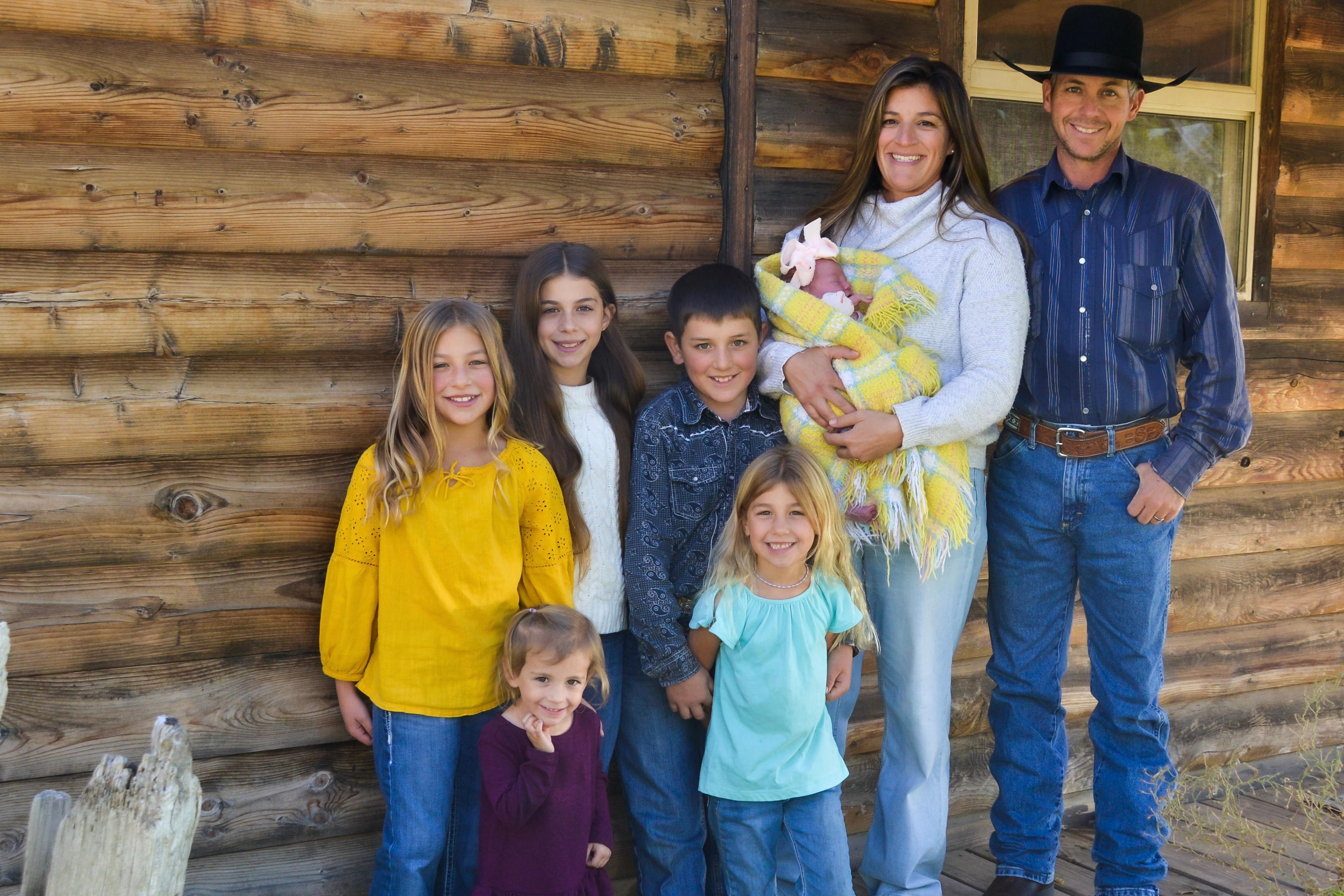 Stephanie and Eric Johnson with their six children in front of a log cabin.