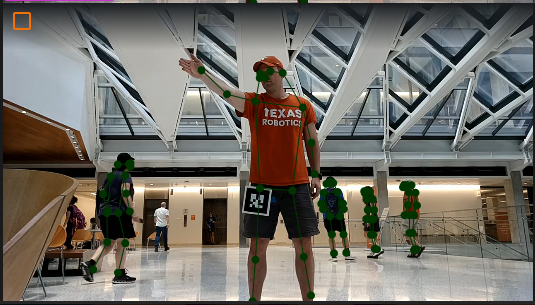 A person performing a gesture in a building lobby, with pose keypoints detected in green on them and on bystanders in the background.