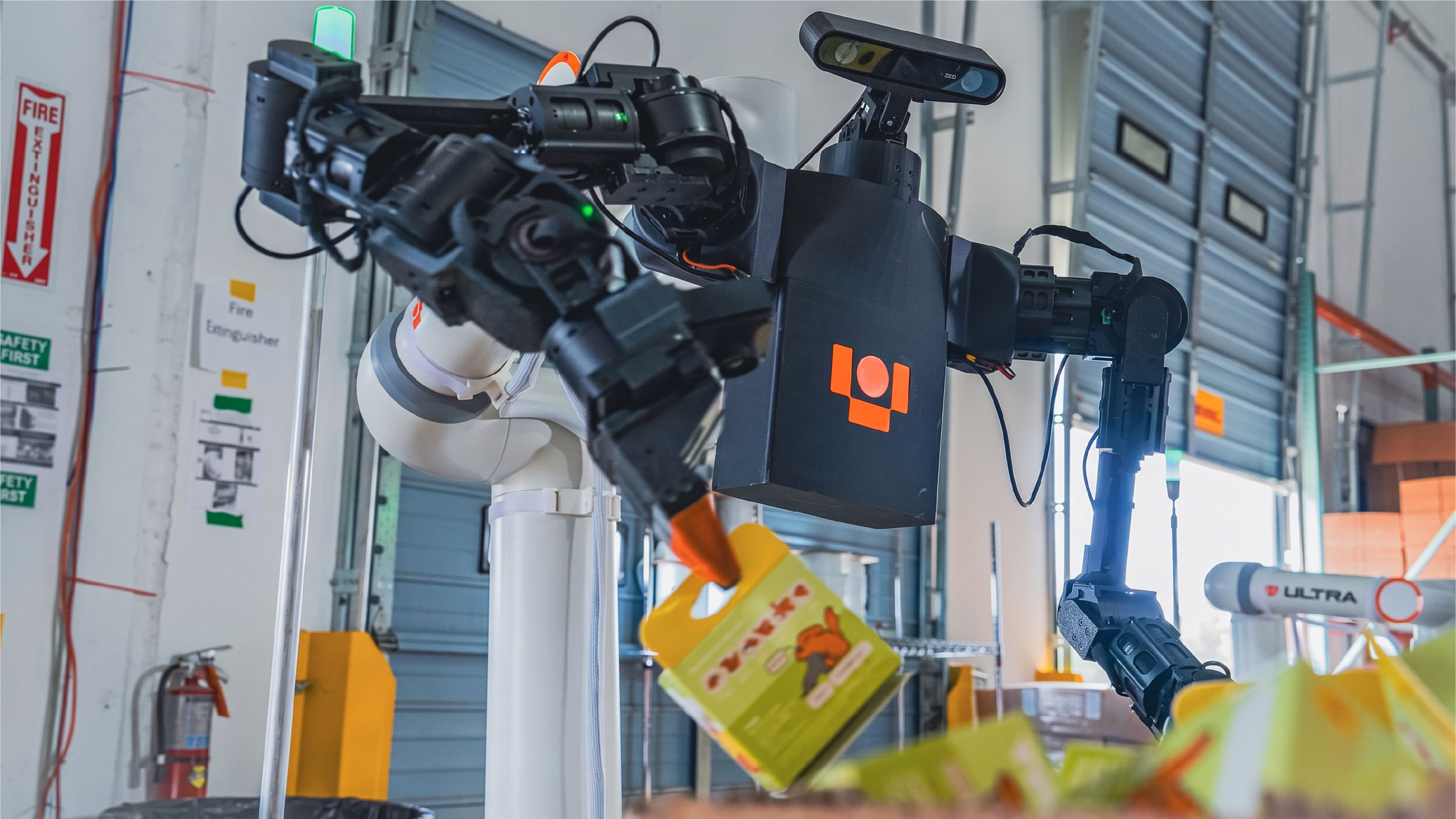 Ultra Robotics' dual-arm OP1 robot handles packaged products at a warehouse facility, with another Ultra robotic arm visible in the background.