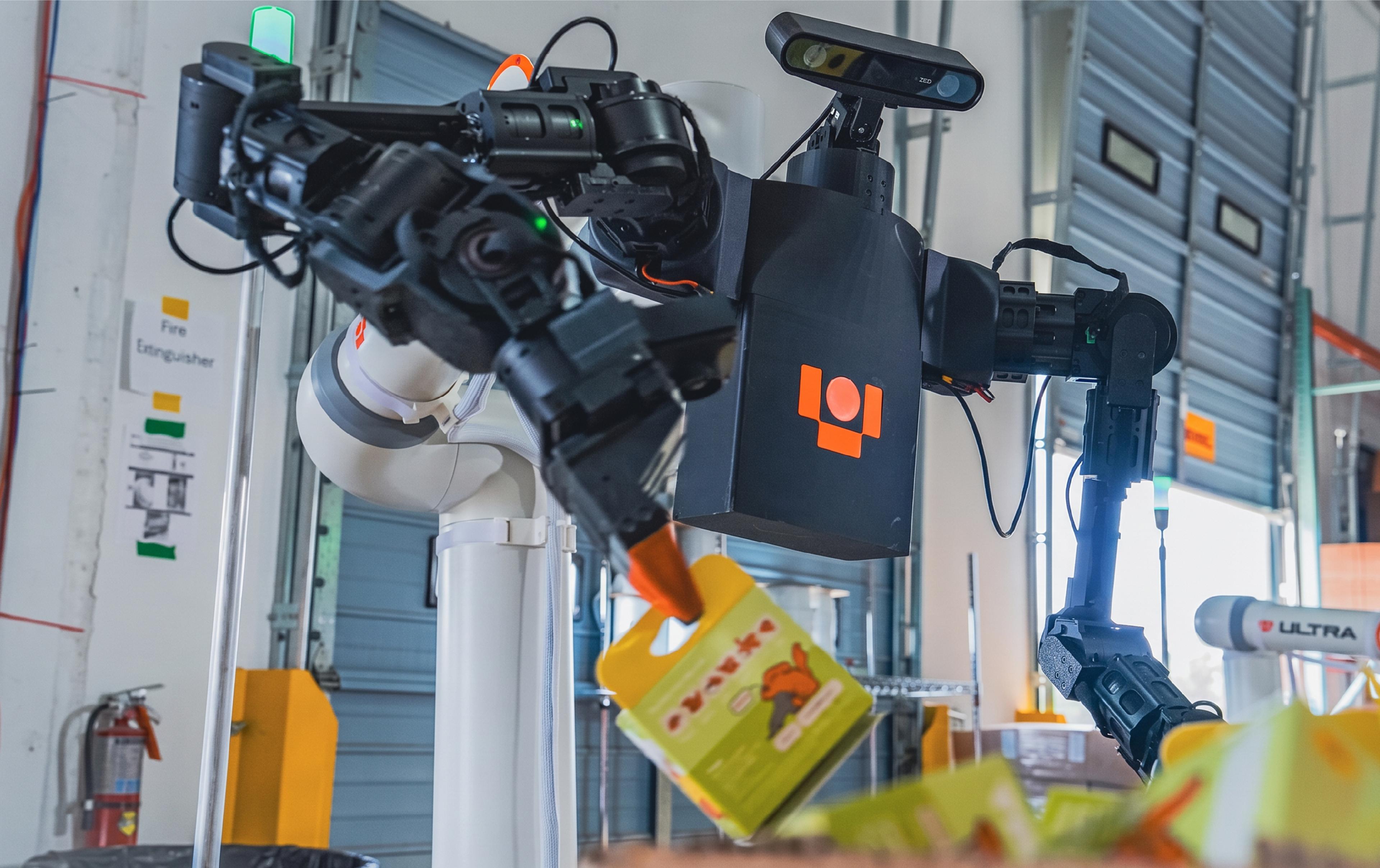 Ultra Robotics' dual-arm OP1 robot handles packaged products at a warehouse facility, with another Ultra robotic arm visible in the background.