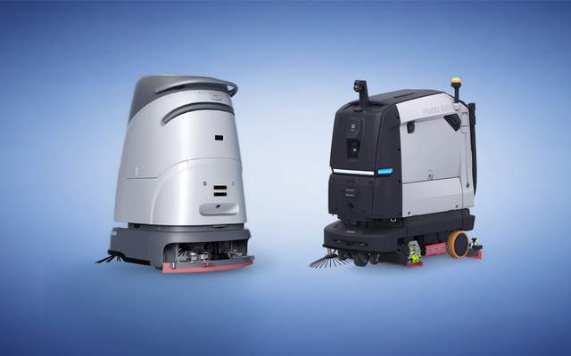 Side-by-side comparison of two commercial cleaning robots on a blue background: VIGGO's compact silver SC50 Pro Plus scrubber on the left, and Pudu Robotics' larger black-and-white BG1 sweeper-scrubber on the right.