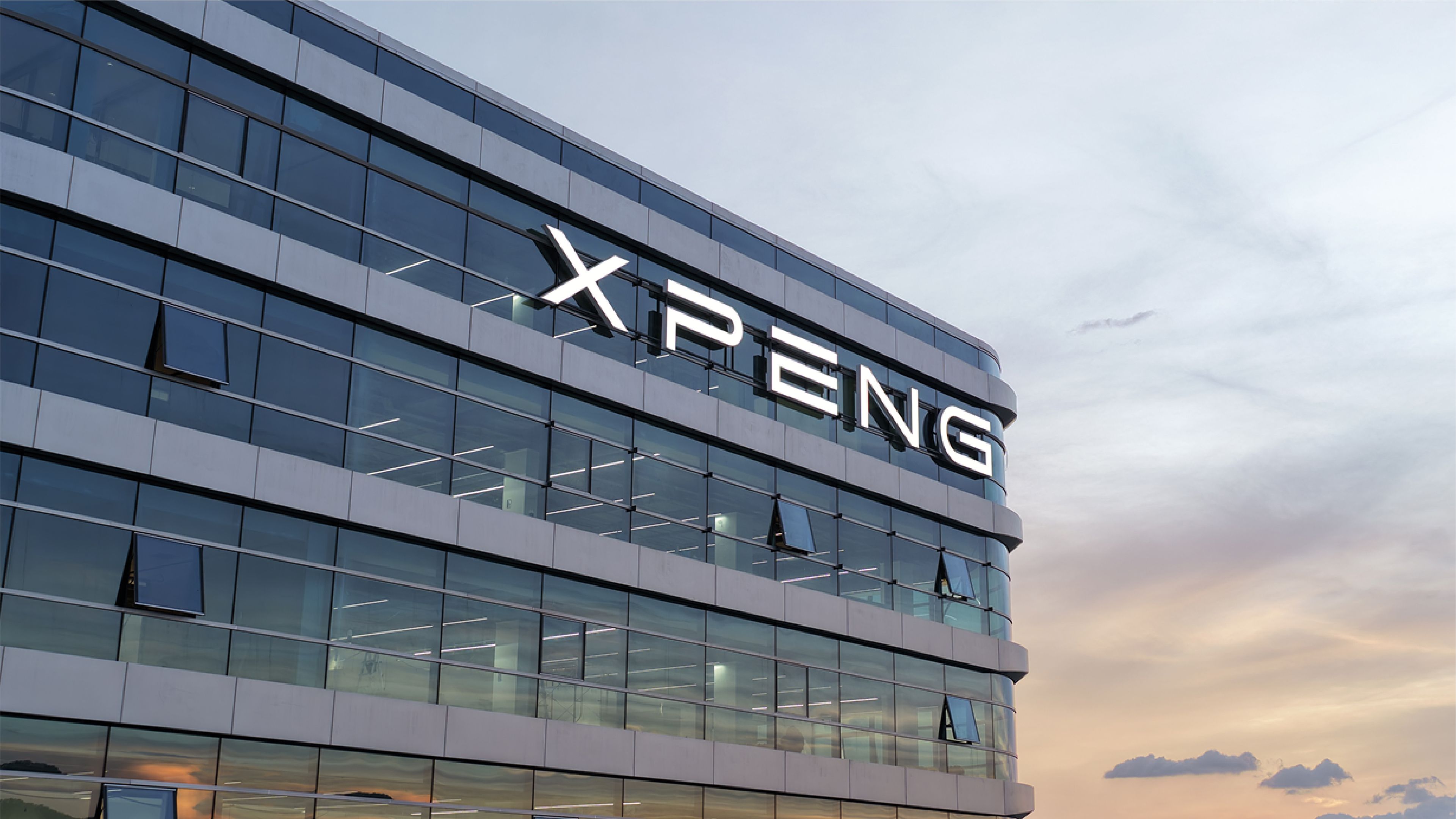 The XPeng logo illuminated on the glass facade of a corporate building at dusk, with a pastel sky in the background.