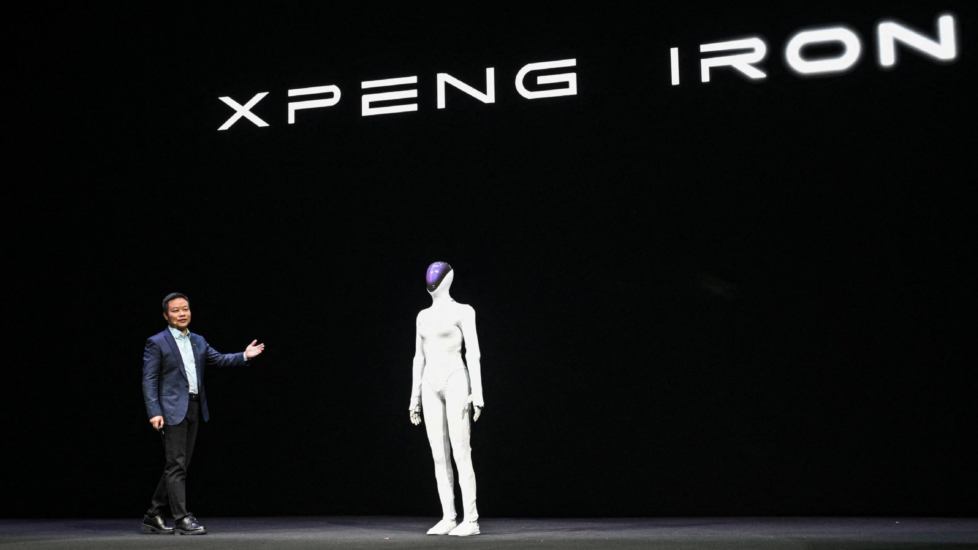 XPENG’s IRON humanoid robot stands onstage beside a company executive during a presentation.