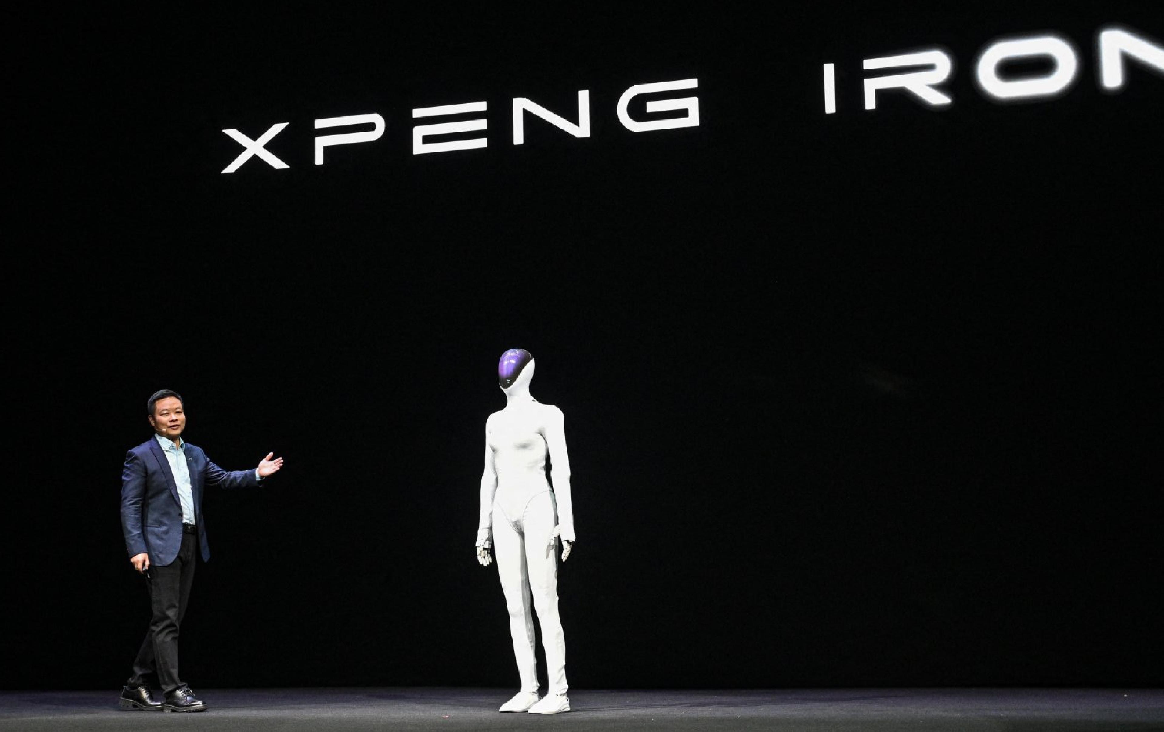 XPENG’s IRON humanoid robot stands onstage beside a company executive during a presentation.