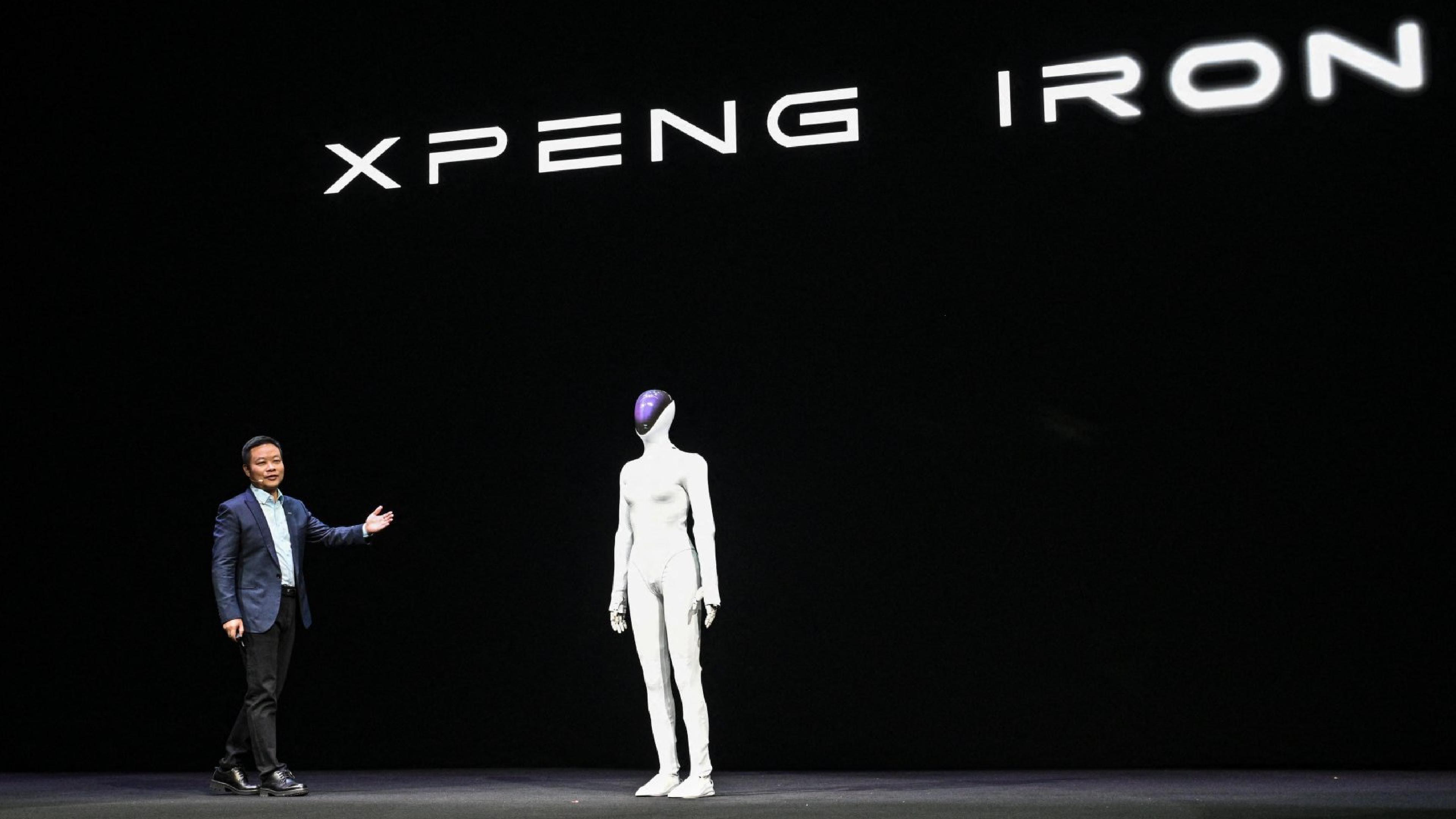 XPENG’s IRON humanoid robot stands onstage beside a company executive during a presentation.