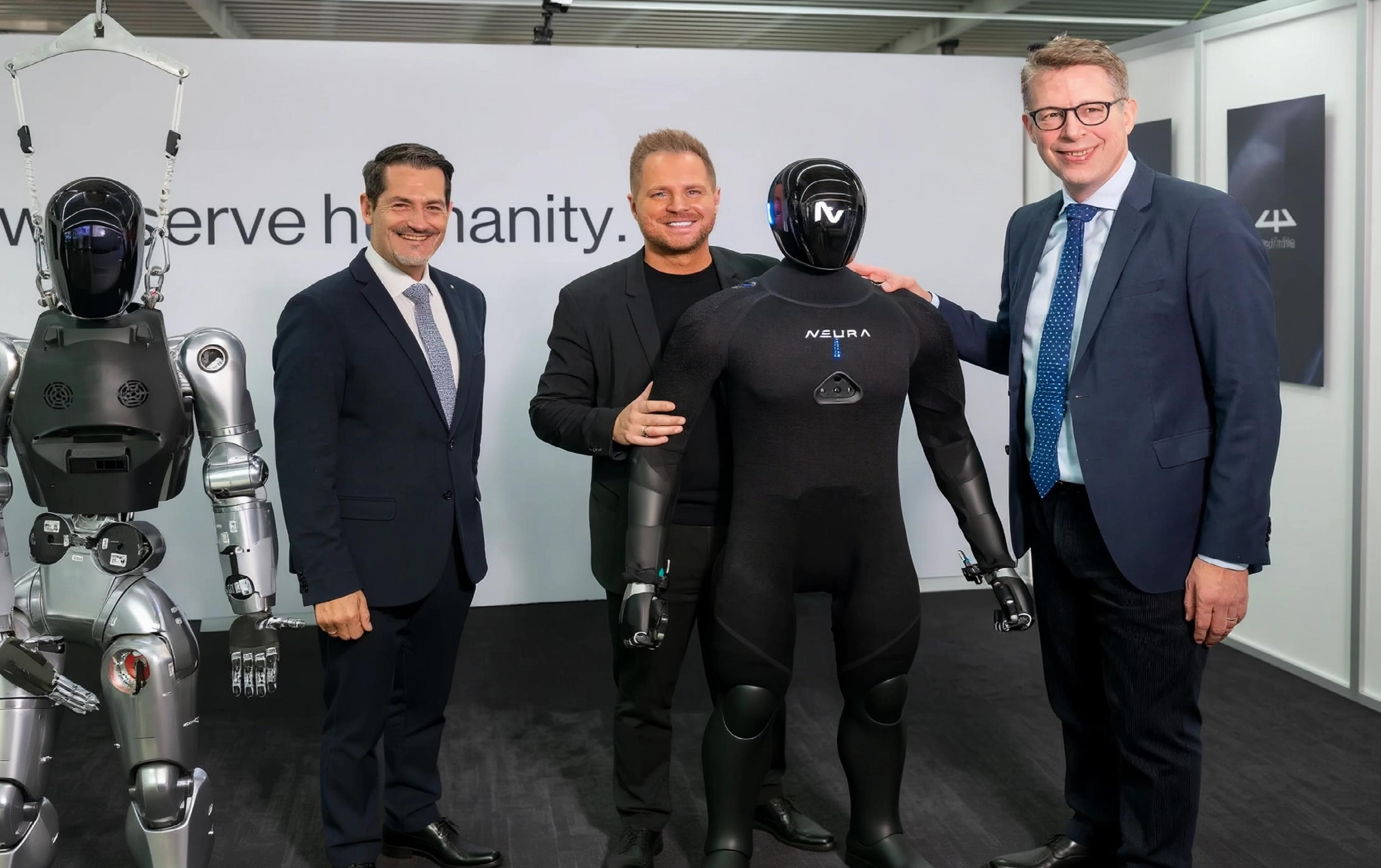 Three men pose with two generations of NEURA Robotics' humanoid robots.