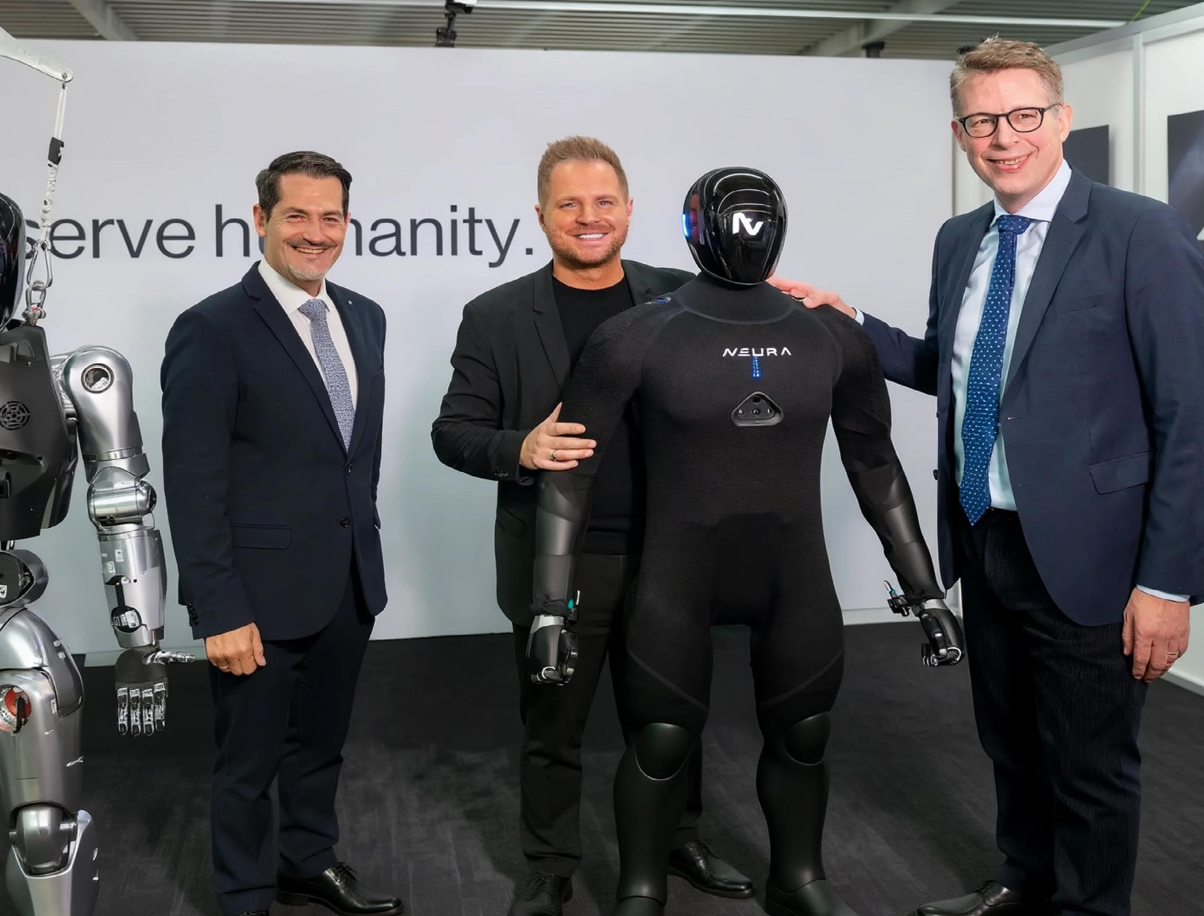 Three men pose with two generations of NEURA Robotics' humanoid robots.