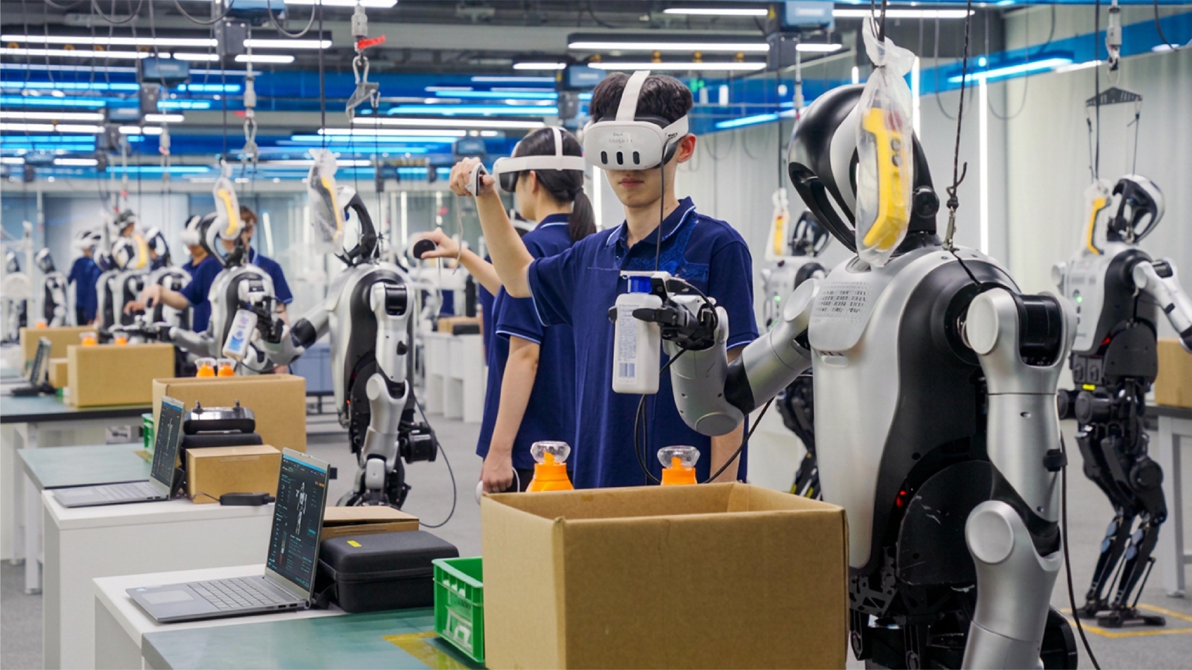 Workers wearing motion-capture headsets and controllers guide humanoid robot arms through box-packing tasks at the Shijingshan Embodied Intelligence Training Center in Beijing, with rows of suspended humanoid robots visible in the background.