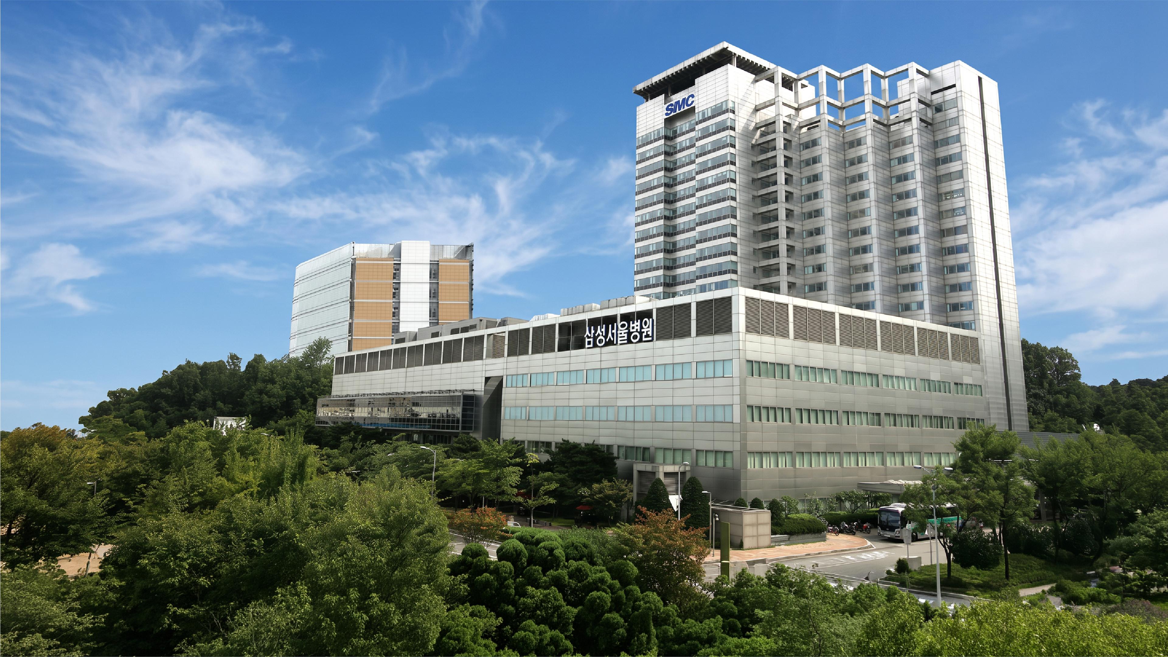 Exterior of Samsung Medical Center in Seoul, South Korea, with tall hospital buildings surrounded by trees under a blue sky.