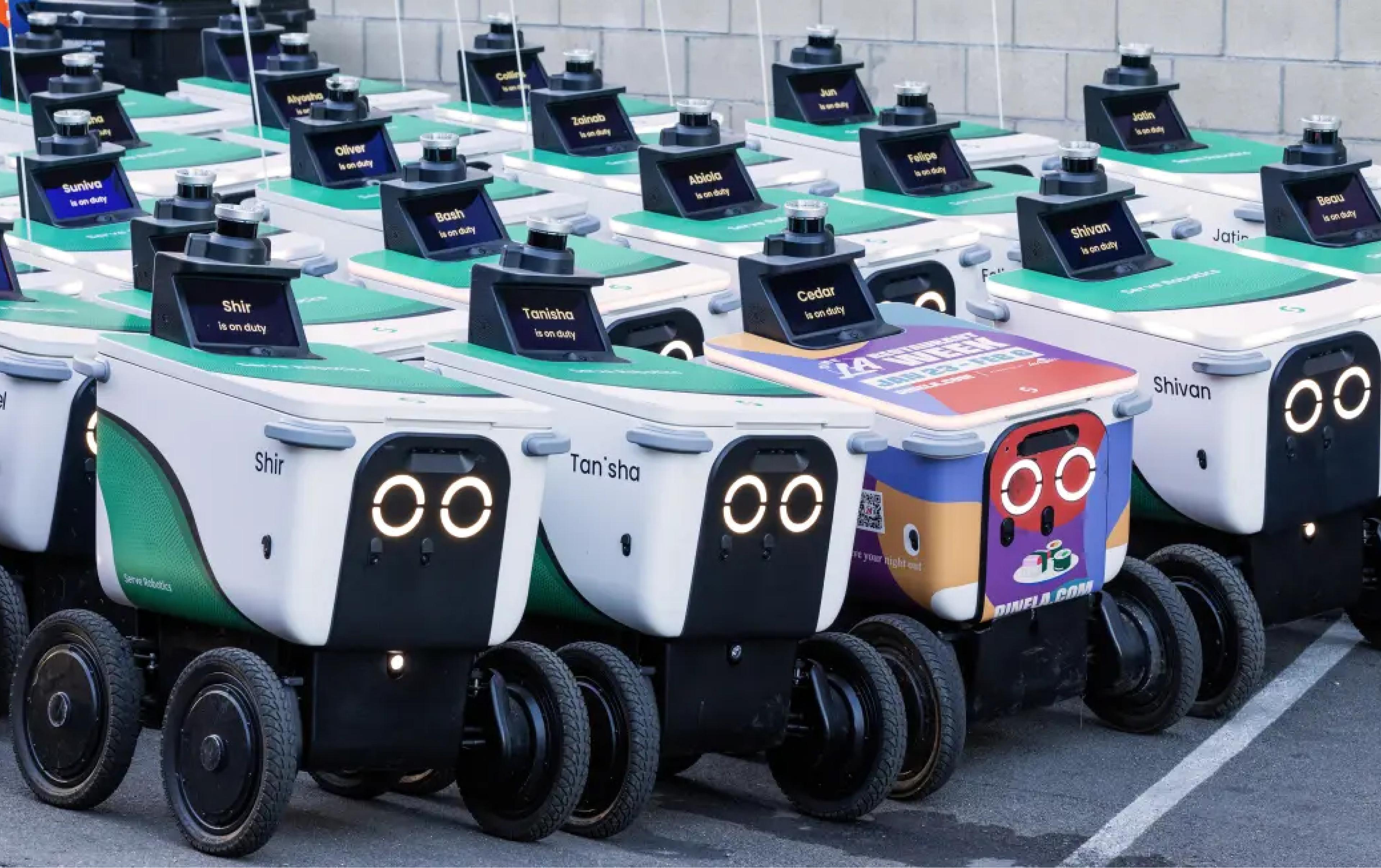 Rows of white sidewalk delivery robots with green lids are parked in tight formation in a parking lot