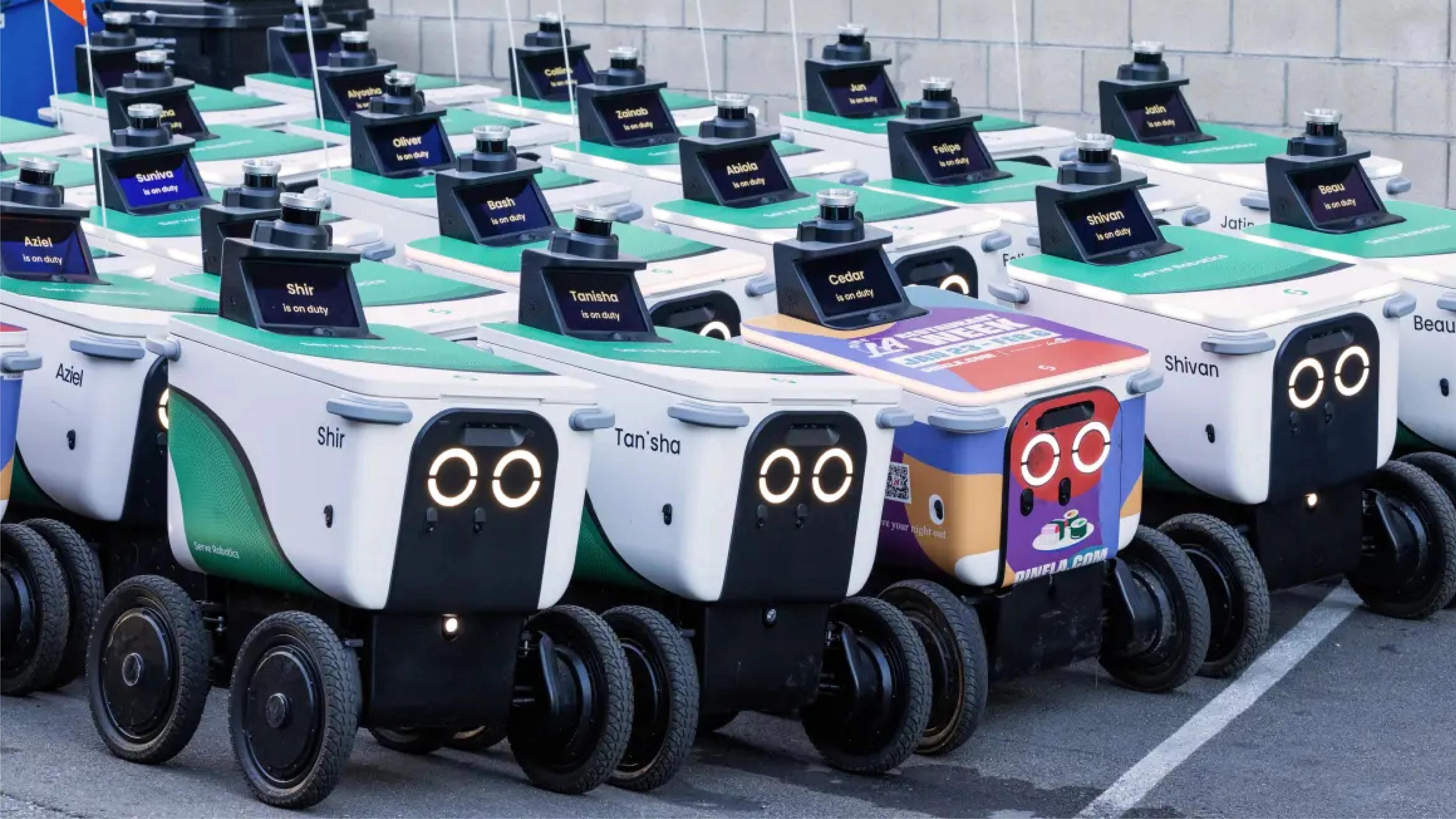Rows of white sidewalk delivery robots with green lids are parked in tight formation in a parking lot