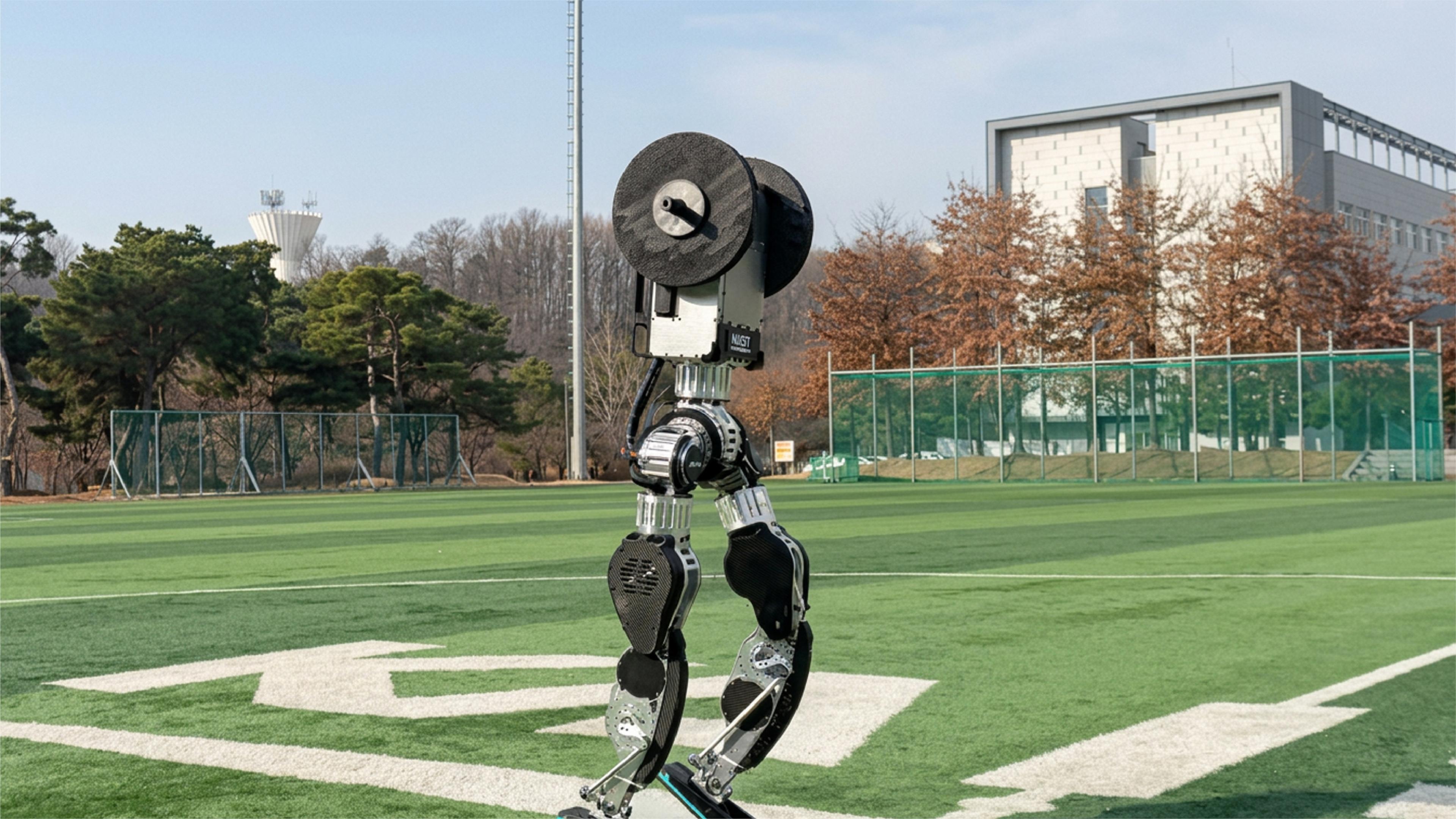 A two-legged walking robot with a circular body moves across an outdoor sports field near in a university.