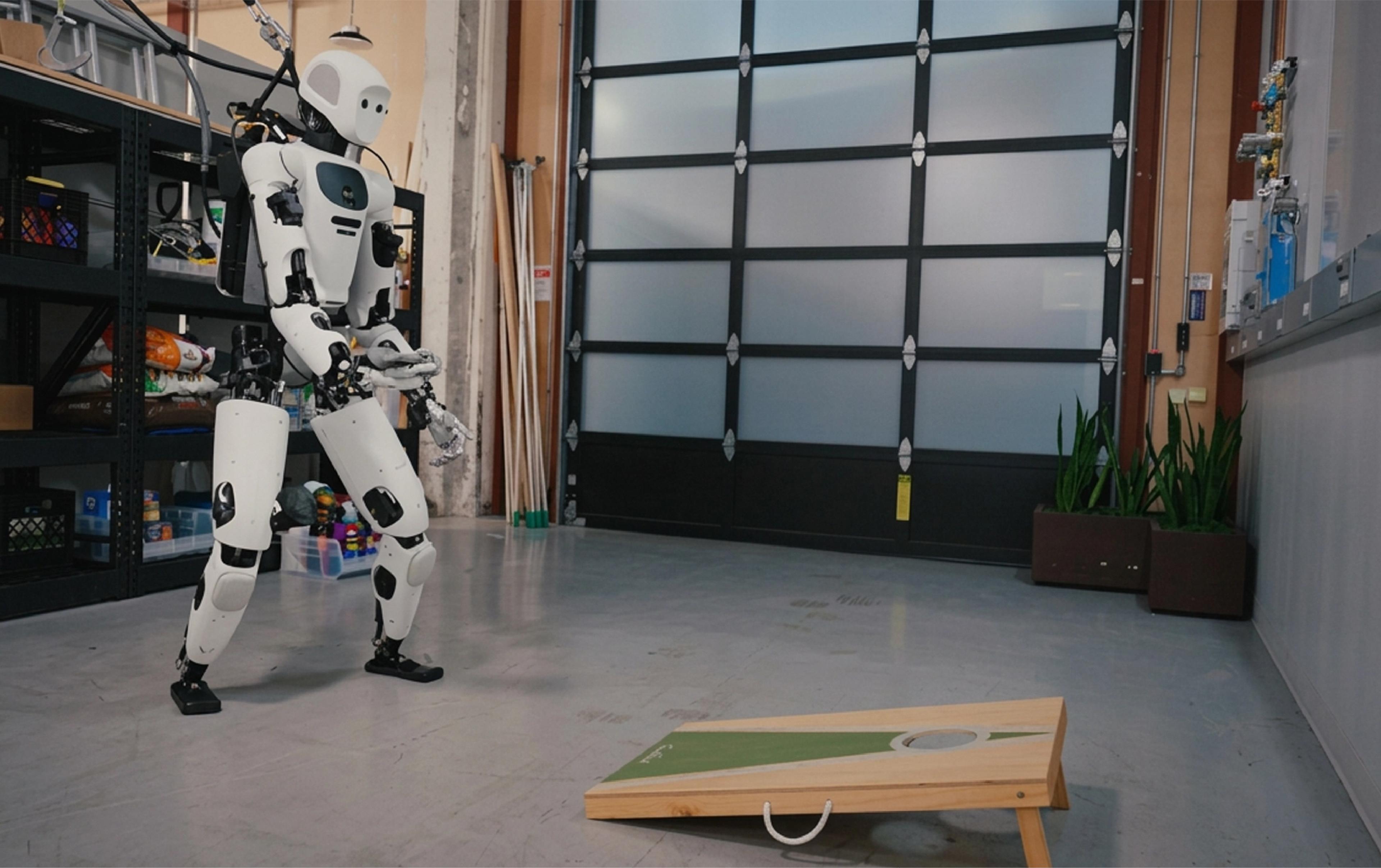 A humanoid robot prepares to throw a beanbag at a cornhole board inside a robotics laboratory.