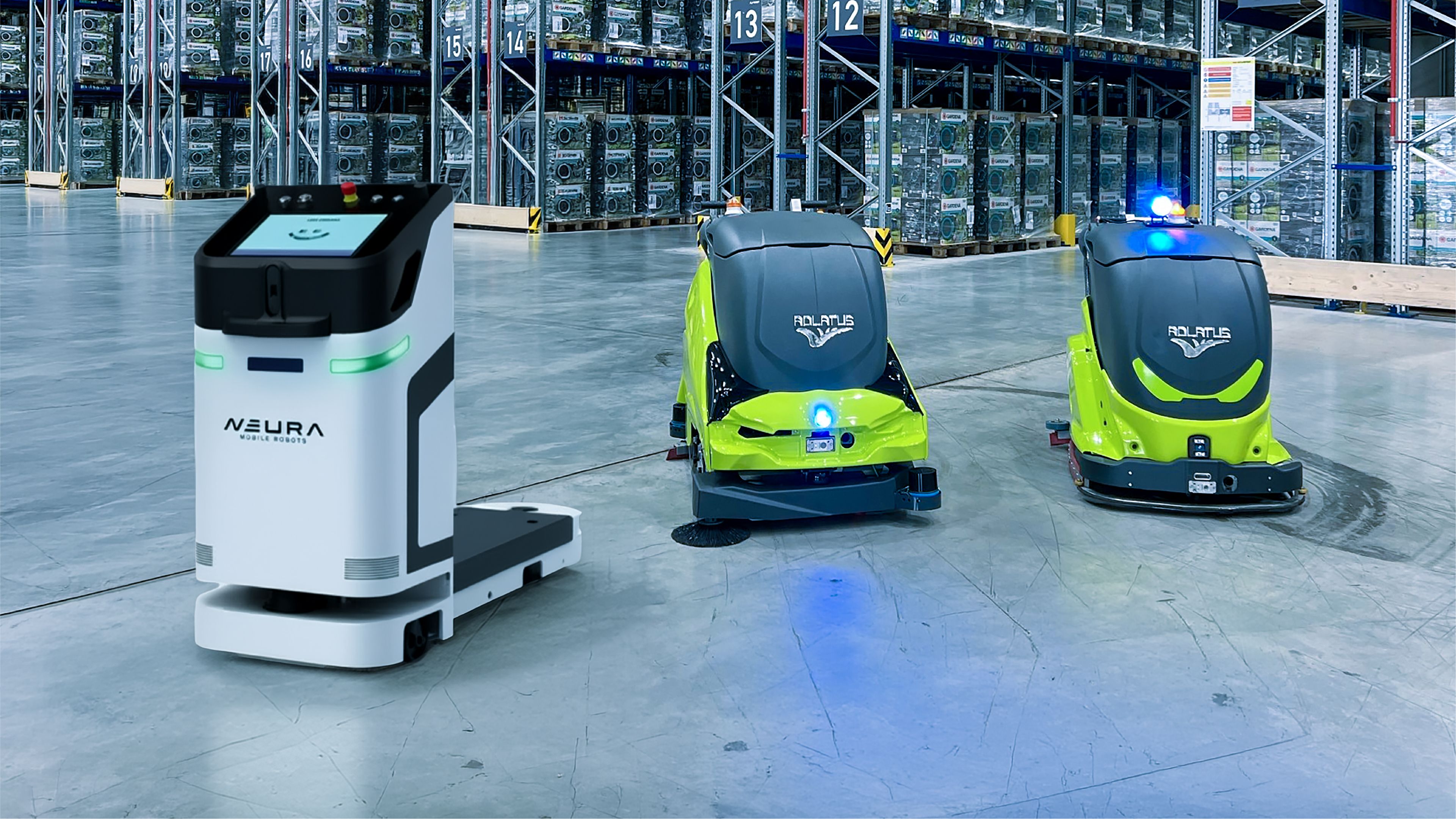 A NEURA logistics robot alongside two green and grey ADLATUS cleaning robots on a warehouse floor lined with tall storage racks.