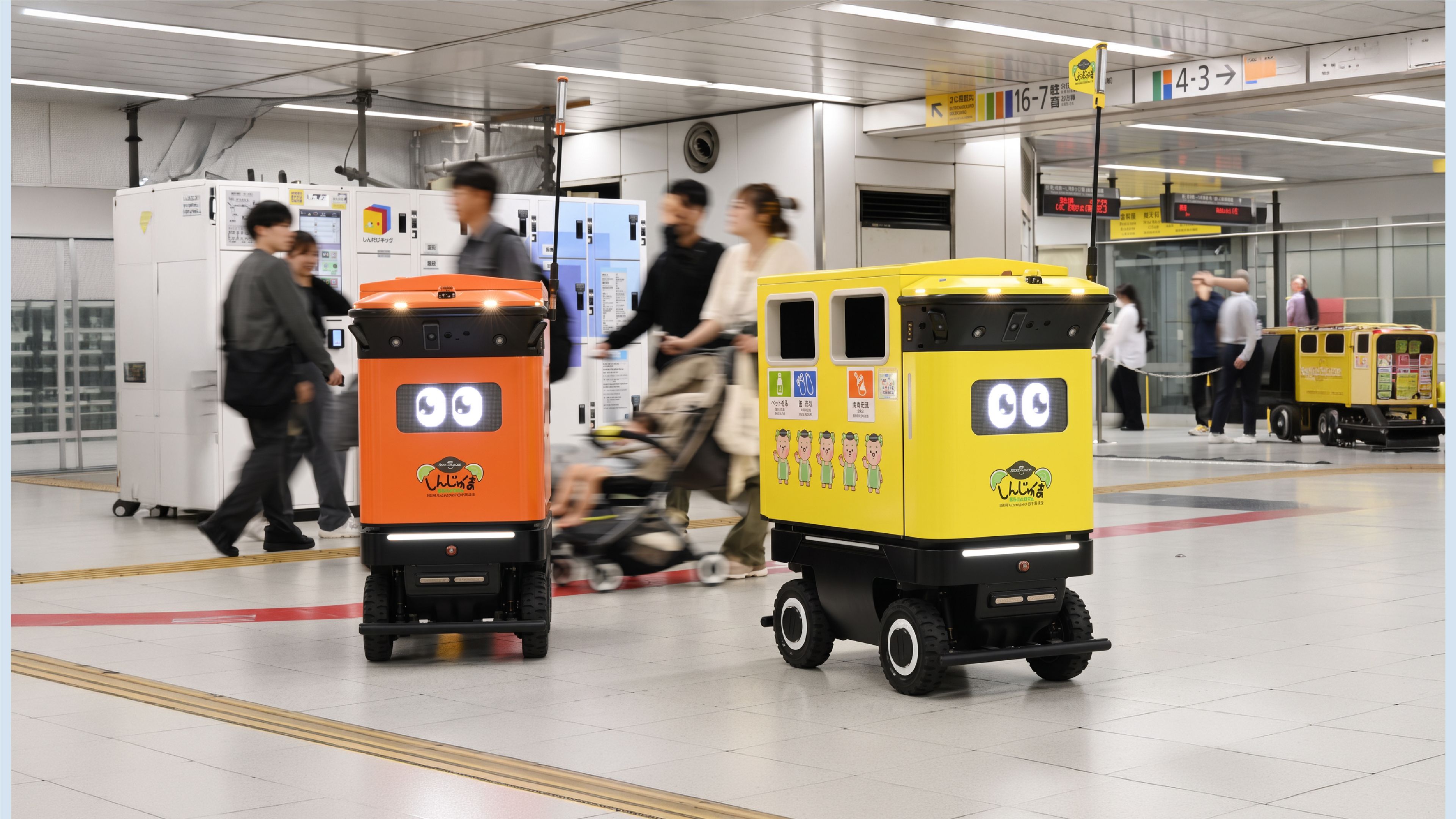 Two autonomous mobile rubbish-collection robots move through a busy Tokyo railway station concourse, with commuters walking and cycling around them.