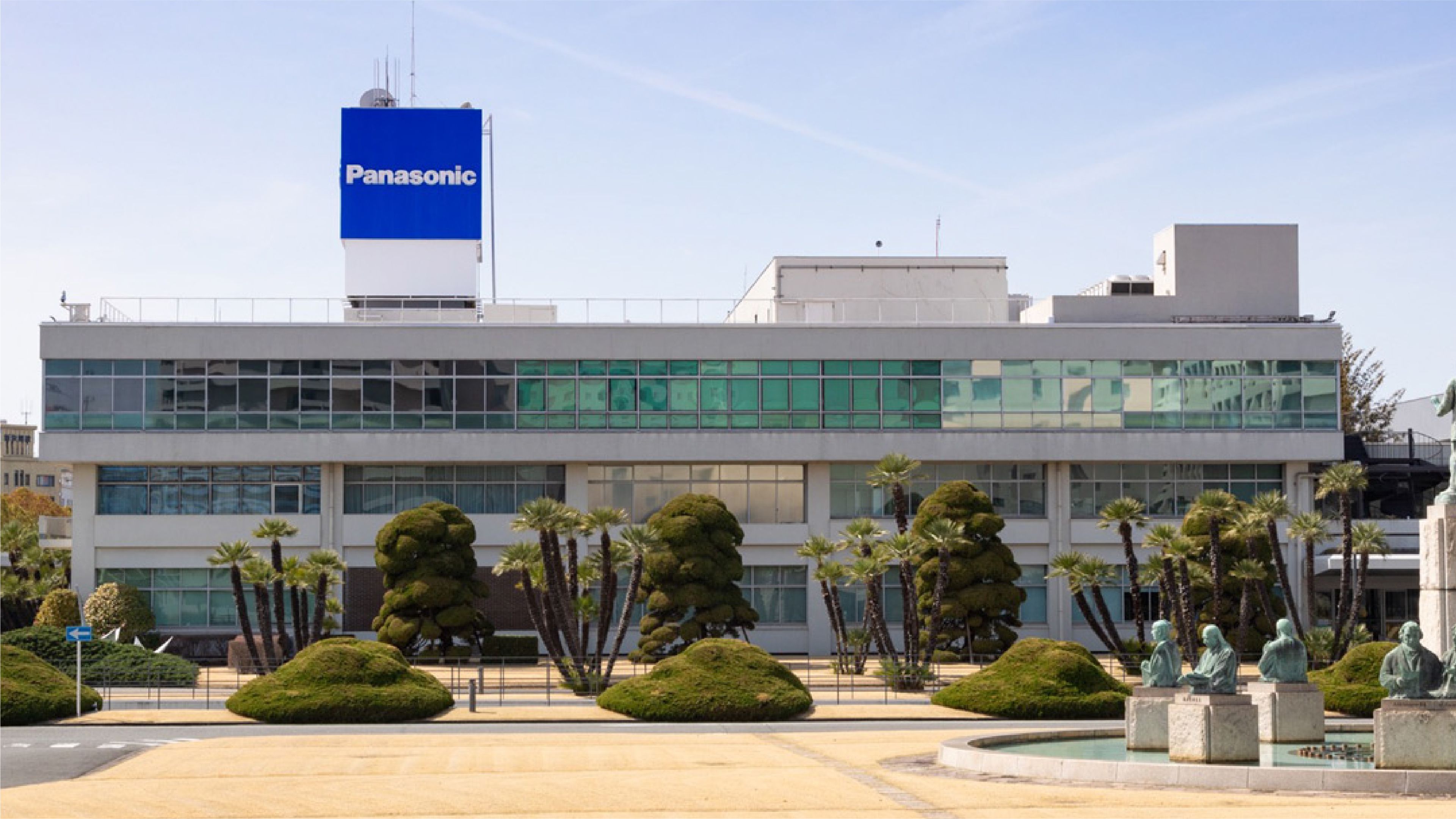 Panasonic building with the company’s blue logo displayed above landscaped grounds and a fountain.