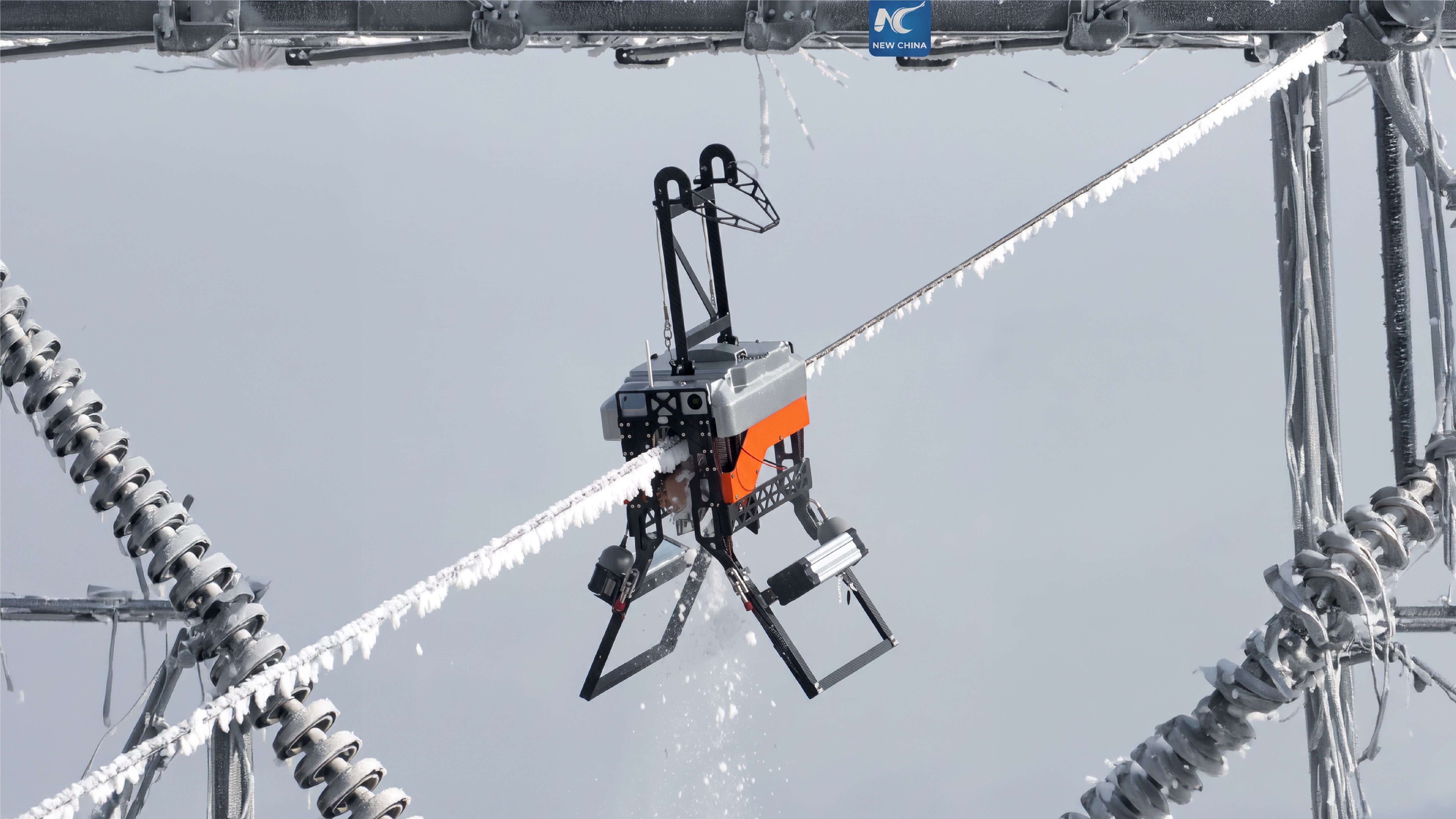 A robot with insect-like articulated legs grips a frost-covered high-voltage power line, suspended between two lattice towers.