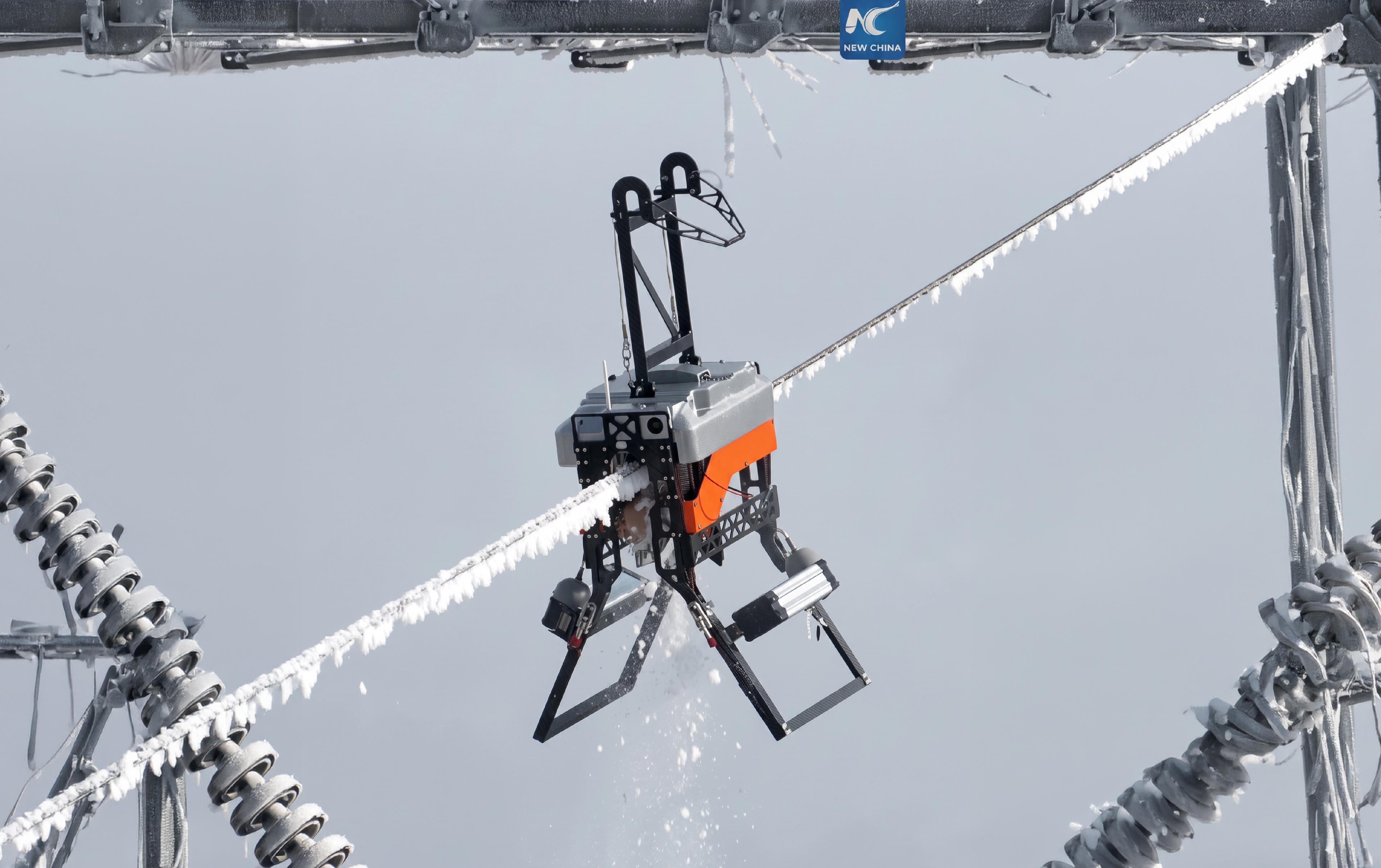 A robot with insect-like articulated legs grips a frost-covered high-voltage power line, suspended between two lattice towers.