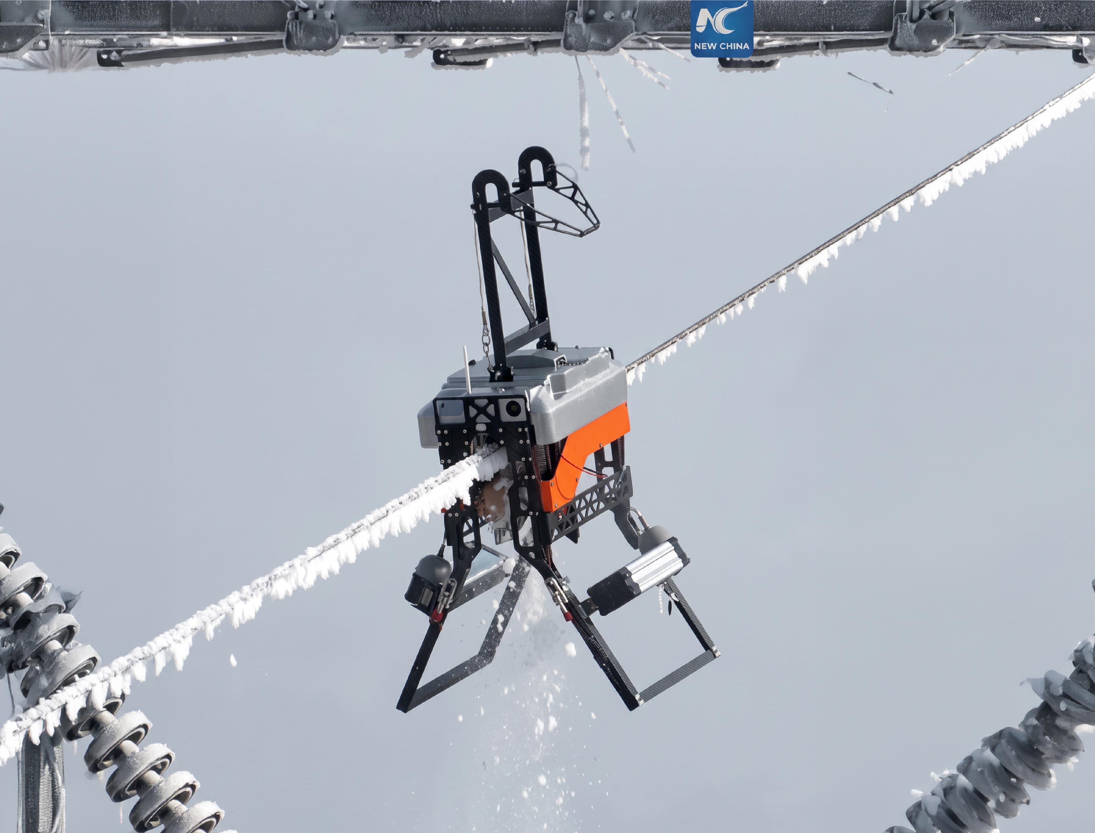 A robot with insect-like articulated legs grips a frost-covered high-voltage power line, suspended between two lattice towers.