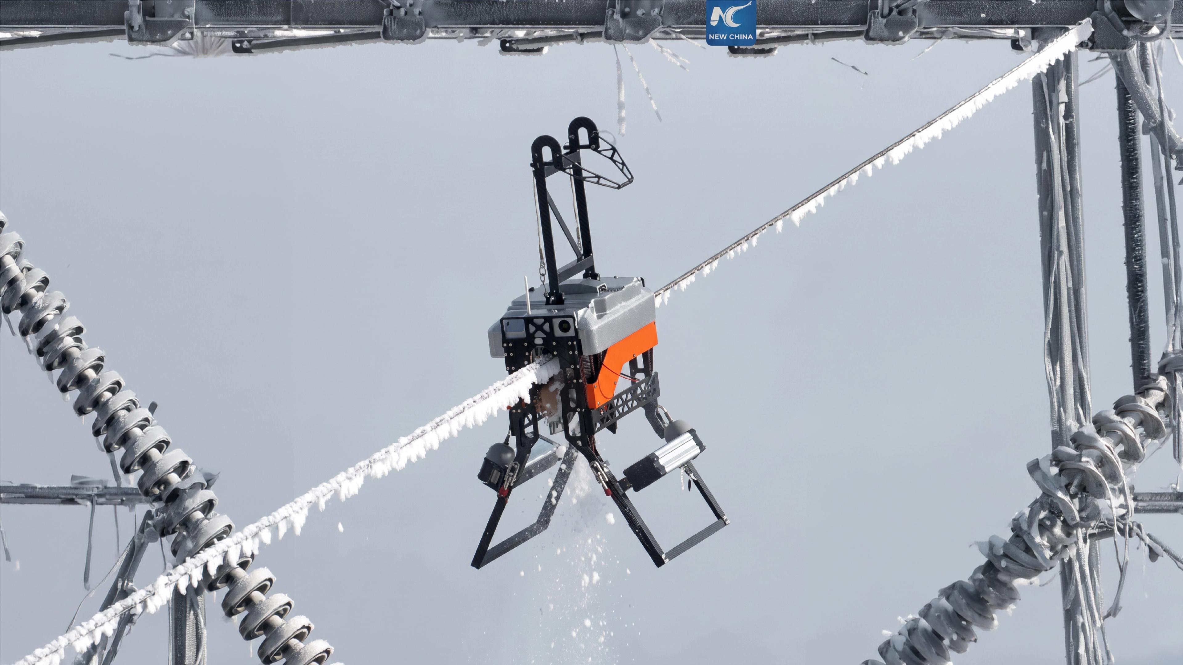 A robot with insect-like articulated legs grips a frost-covered high-voltage power line, suspended between two lattice towers.