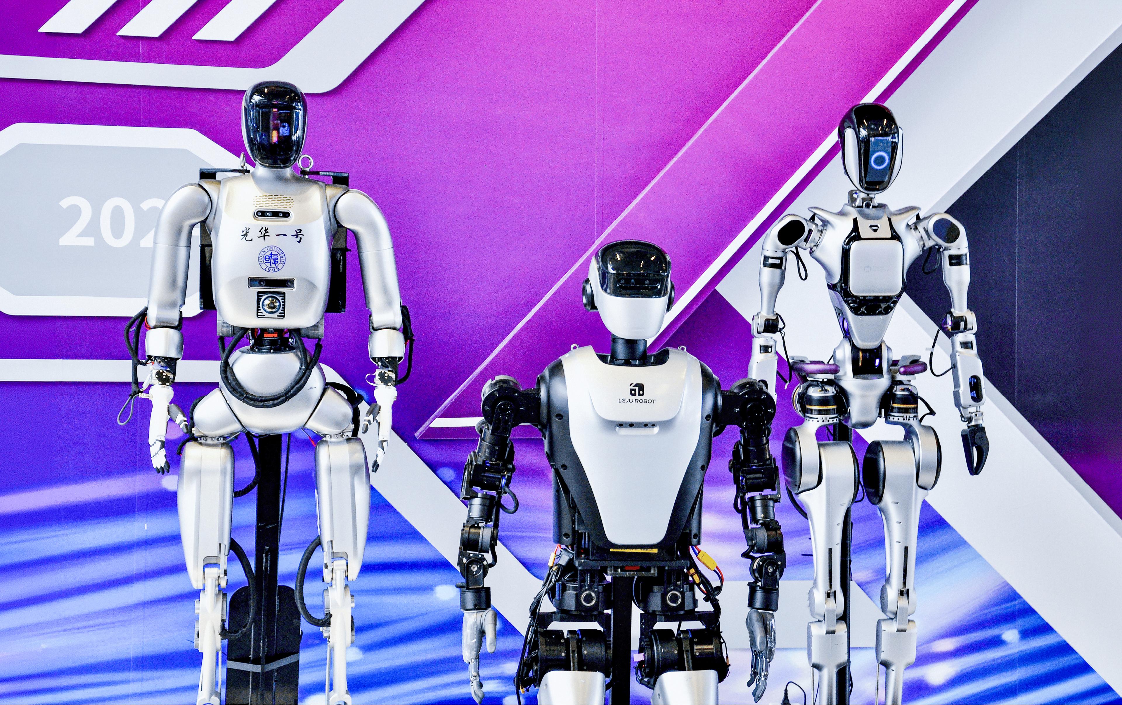 Three humanoid robots on display at a tech expo, from Peking University and one branded Leju Robot, against a purple and white event backdrop