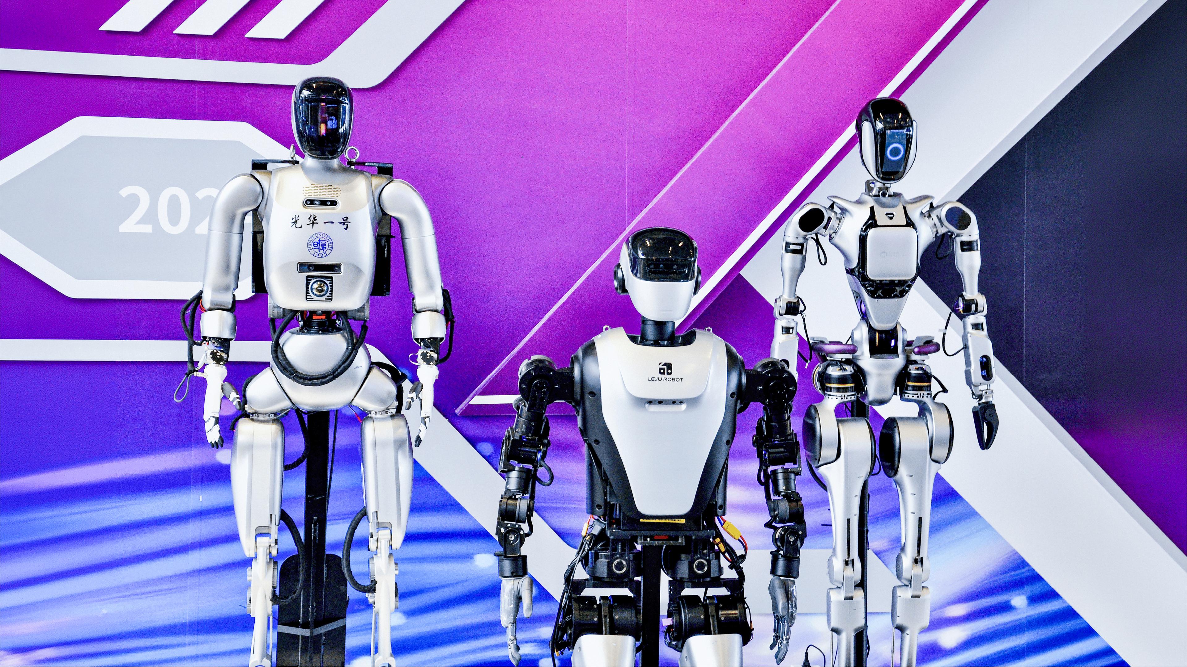 Three humanoid robots on display at a tech expo, from Peking University and one branded Leju Robot, against a purple and white event backdrop