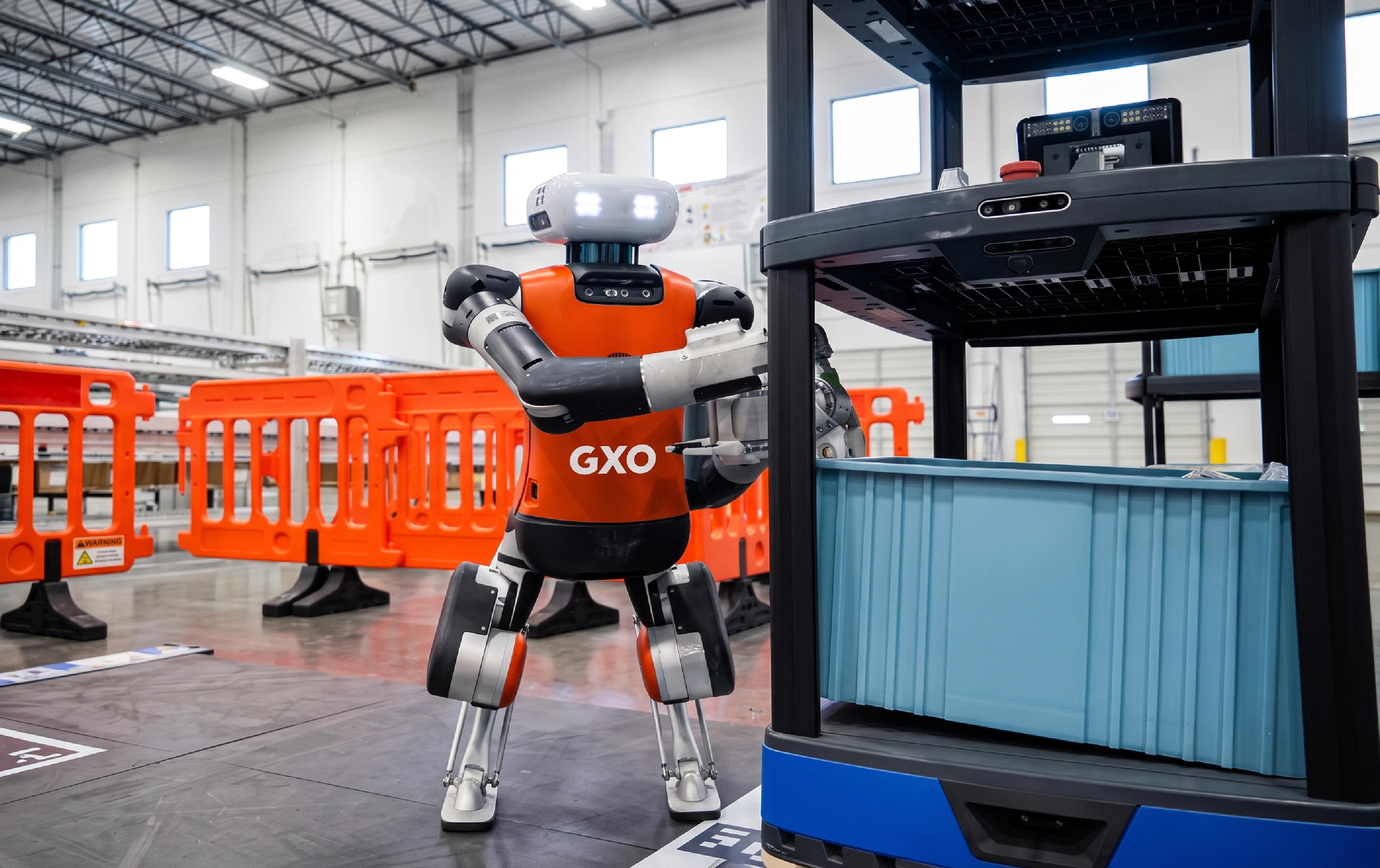 Agility Robotics' Digit humanoid robot, wearing GXO branding, handles a storage tote at a warehouse facility.