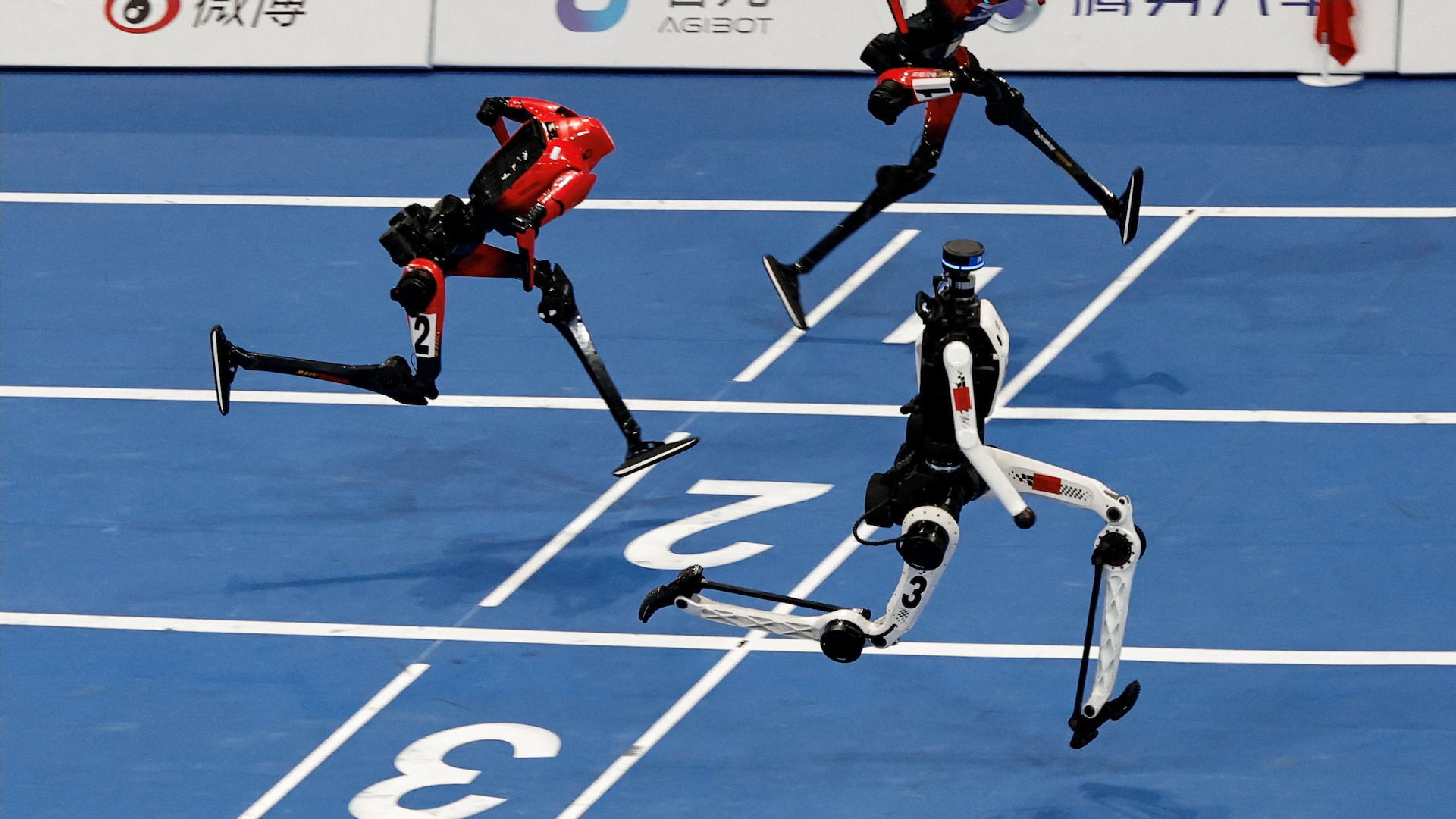 Three humanoid robots sprint side by side on an indoor blue running track, captured mid-stride in a high-tech robot race