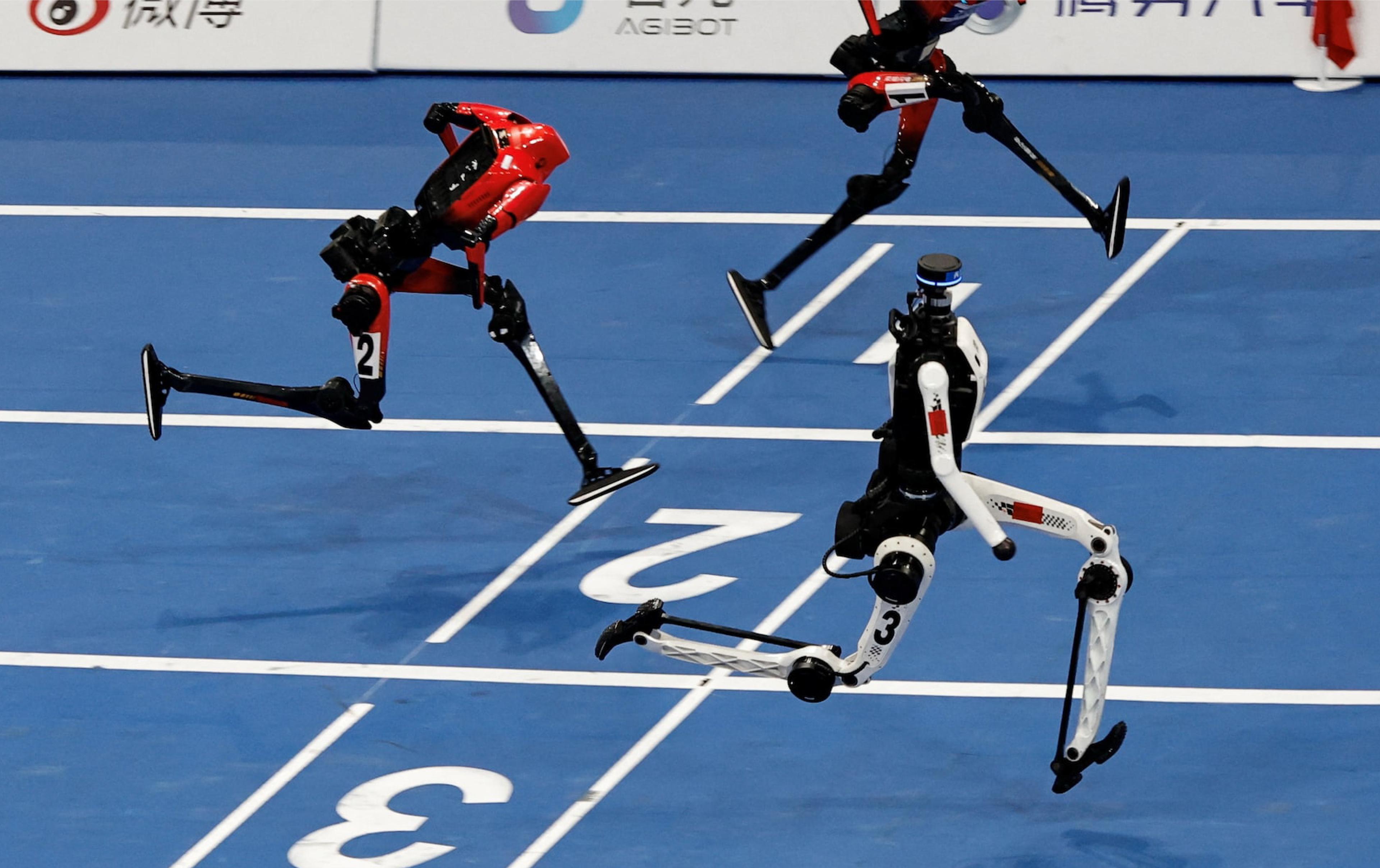 Three humanoid robots sprint side by side on an indoor blue running track, captured mid-stride in a high-tech robot race