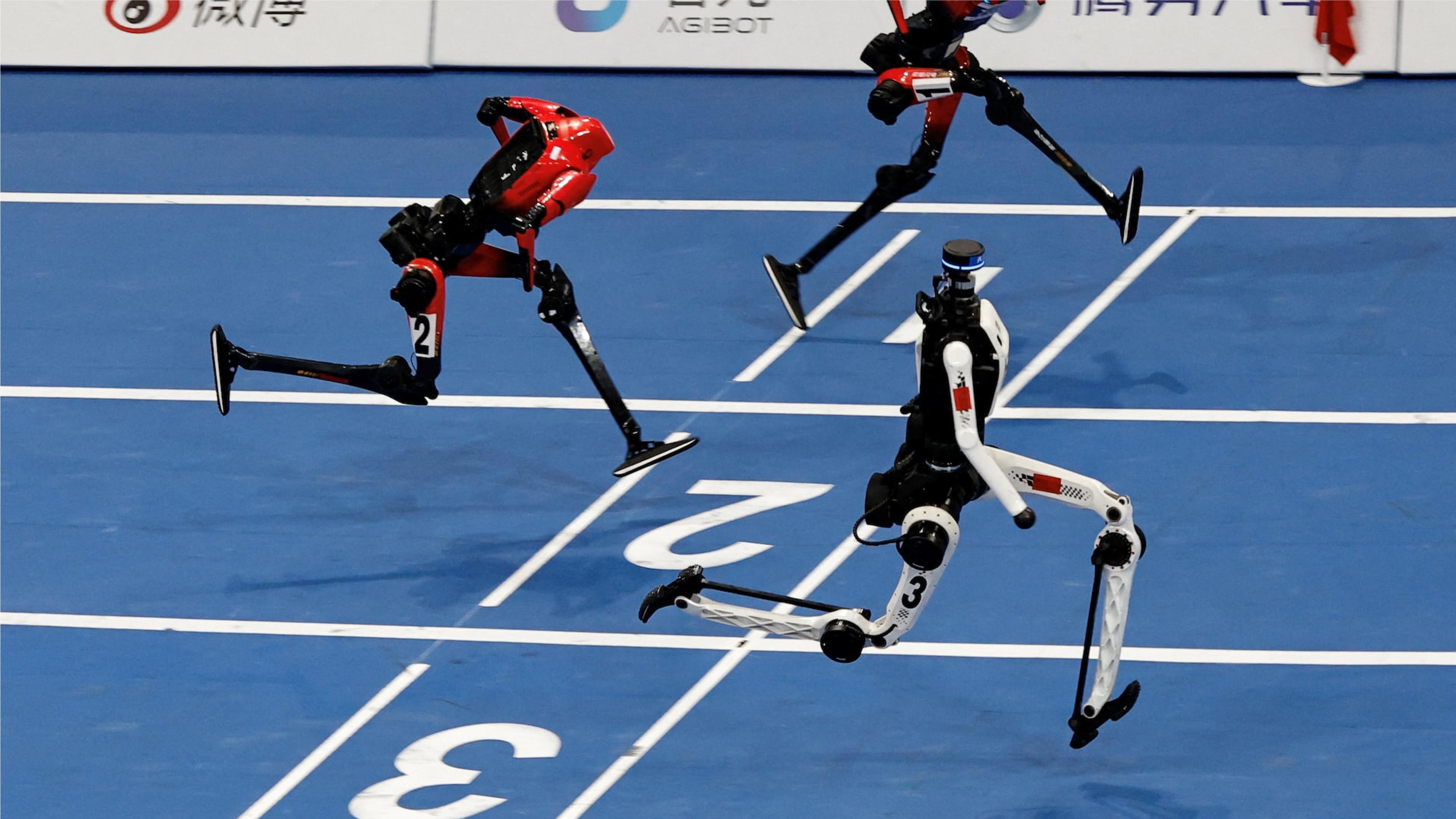 Three humanoid robots sprint side by side on an indoor blue running track, captured mid-stride in a high-tech robot race